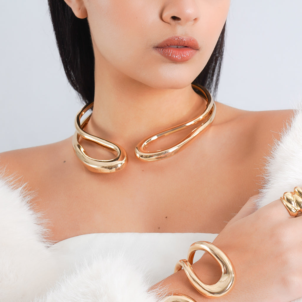 A confident woman with sleek, pulled-back hair poses with her hands framing her face, highlighting bold silver jewelry.