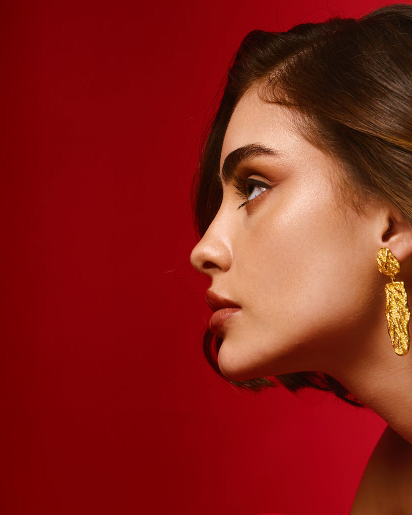 A woman wearing a 18K gold plated earring, showcasing its elegant design against her hair.