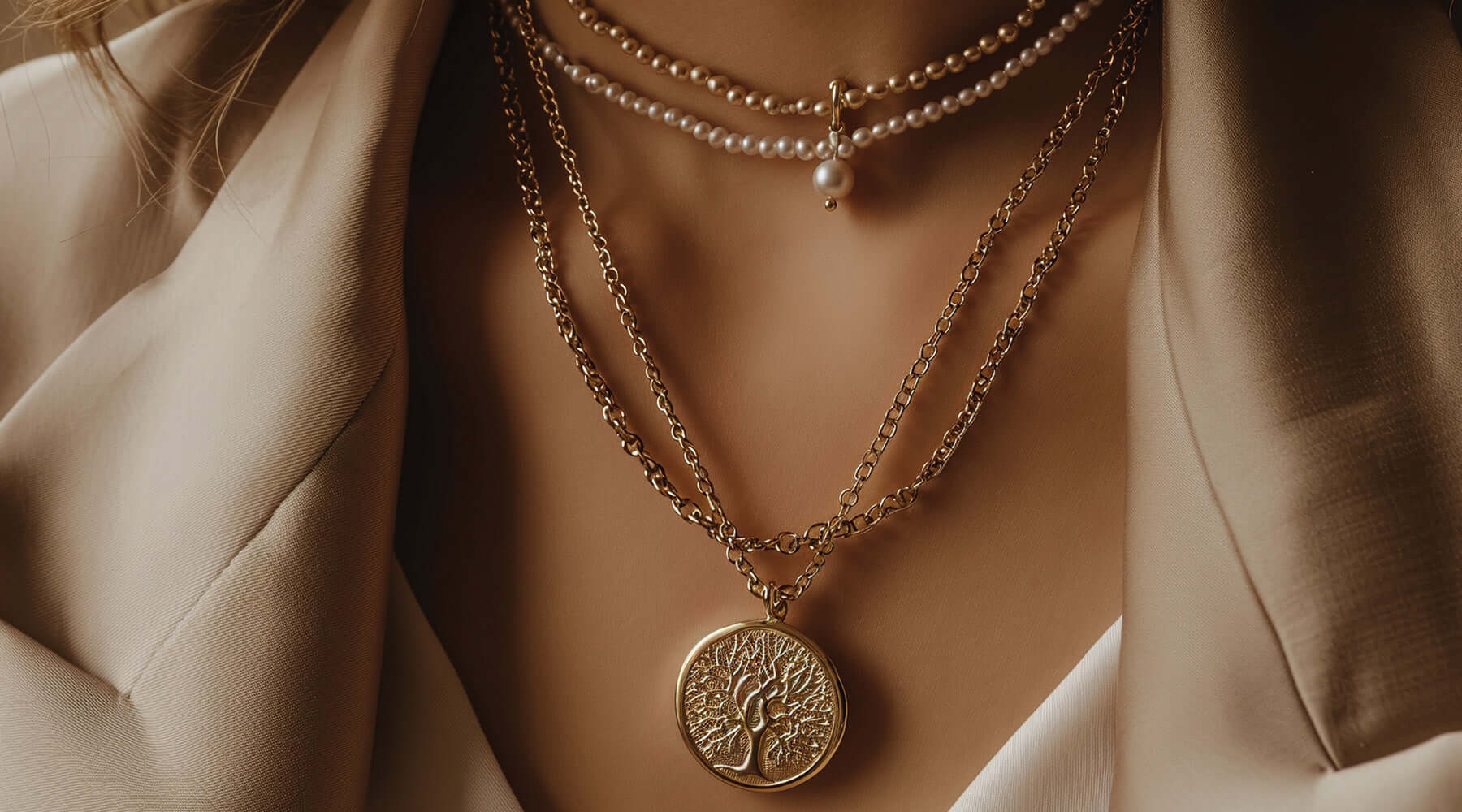 Close up of a layered necklace set featuring delicate 18K gold plated chains and pearls, adorned with a gold pendant showcasing a tree motif, styled elegantly against a beige blazer.