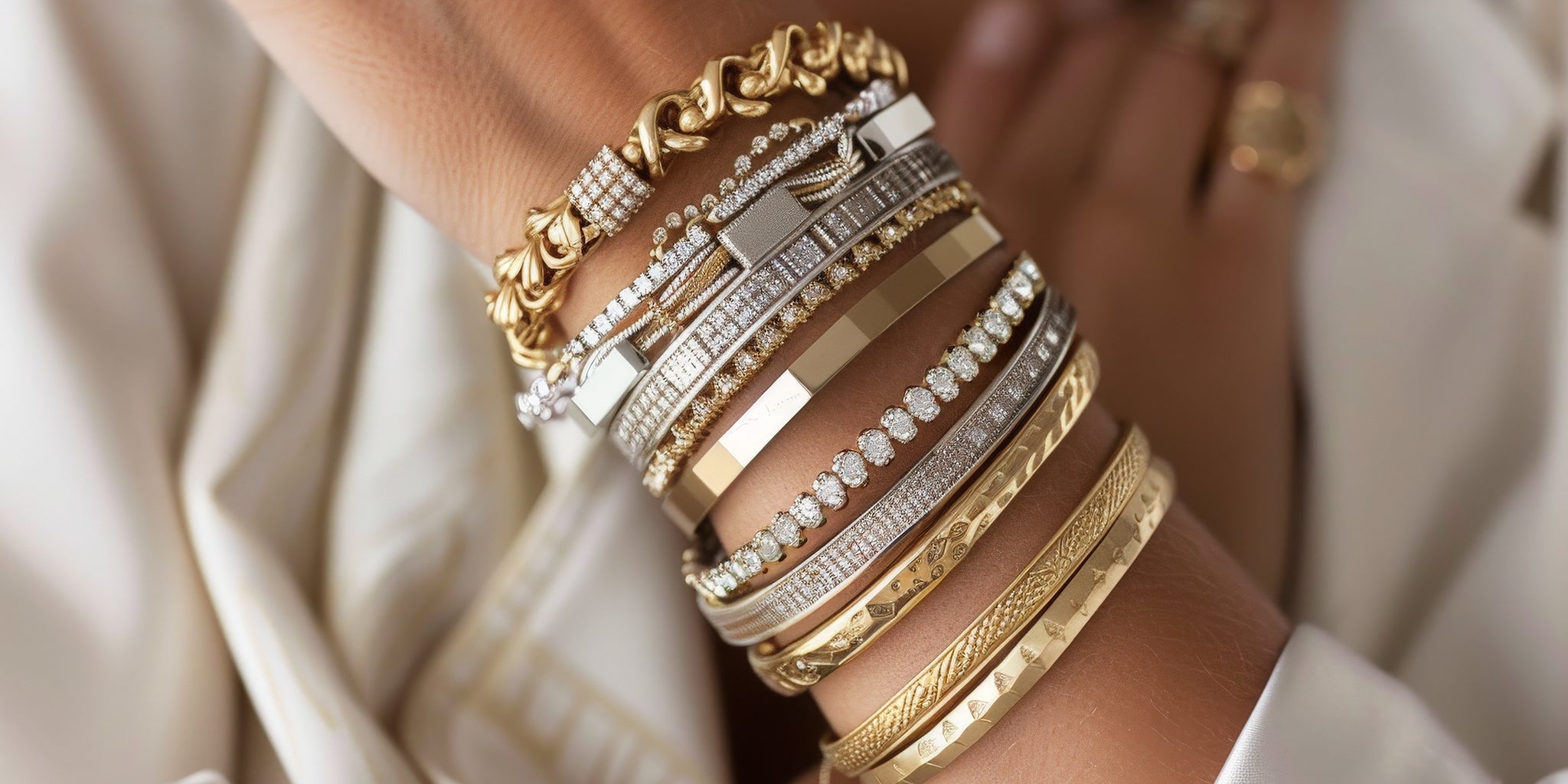 A woman’s wrist stacked with multiple 18K gold-plated bangles, bracelets, and cuffs in stainless steel and brass base, featuring chain links, geometric designs, and diamond-like embellishments — showcasing luxury wrist jewellery styling.