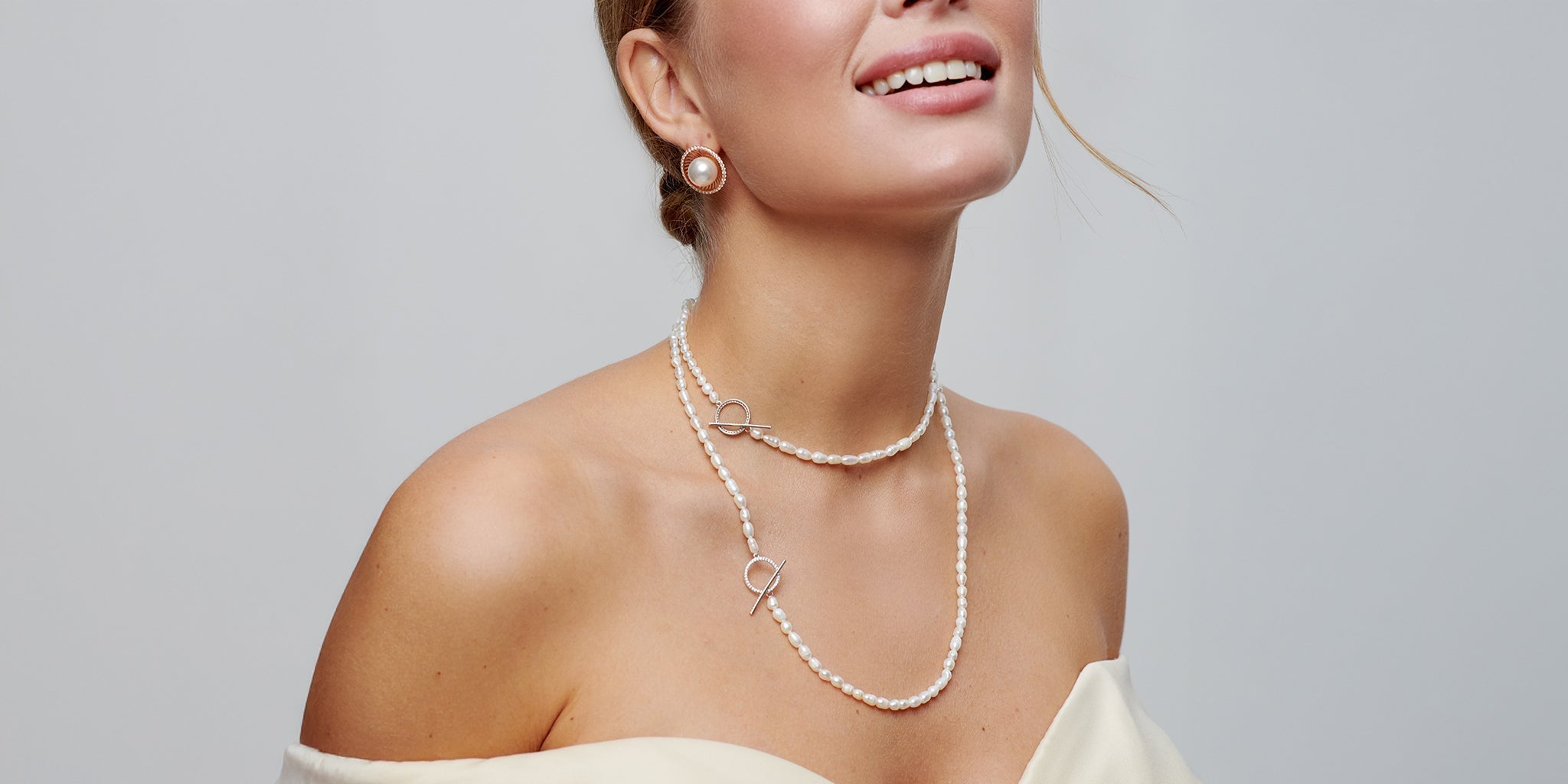 Woman wearing an off-shoulder ivory dress styled with 18K gold-plated pearl drop earrings and a layered pearl necklace featuring delicate circular accents, exuding elegant vintage charm.