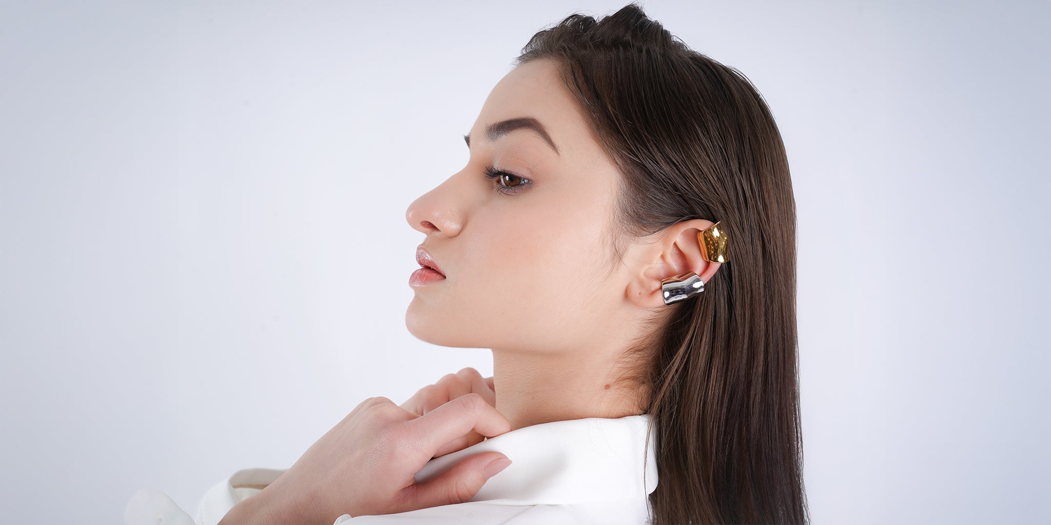 Woman wearing a stylish 18K gold and stainless steel ear cuff, showcasing a modern and elegant jewelry look with sleek hair and a white outfit.
