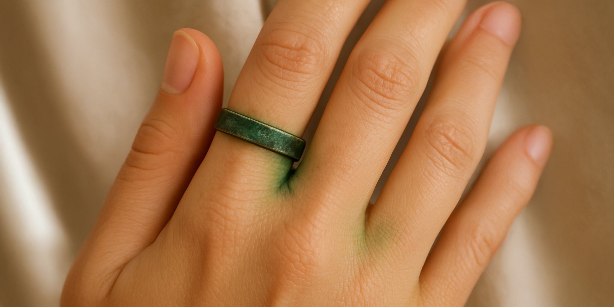 A close-up of a woman’s hand with a stainless steel ring on her middle finger, showing green discoloration on the skin around the ring from tarnishing.