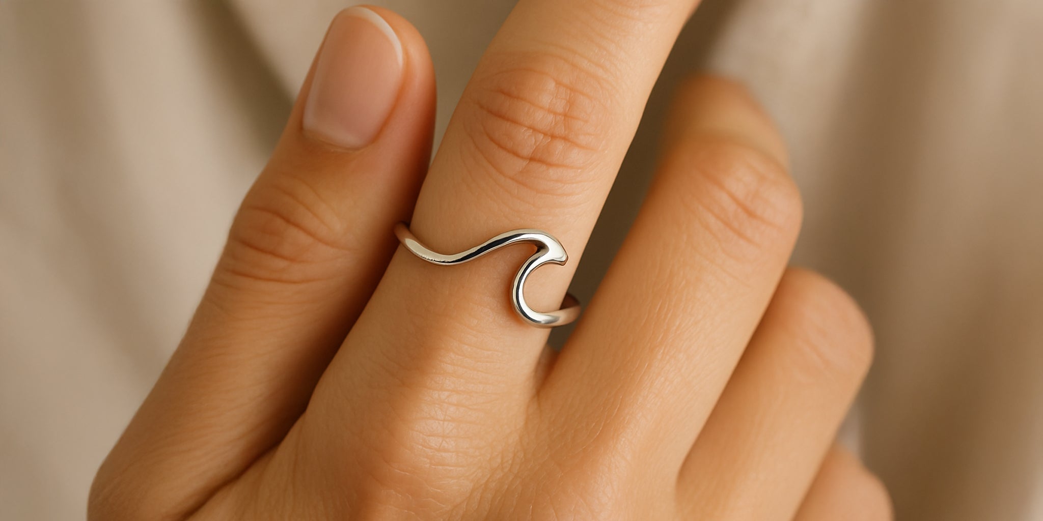 A close-up of a woman’s hand wearing a minimalist wave ring on her finger.