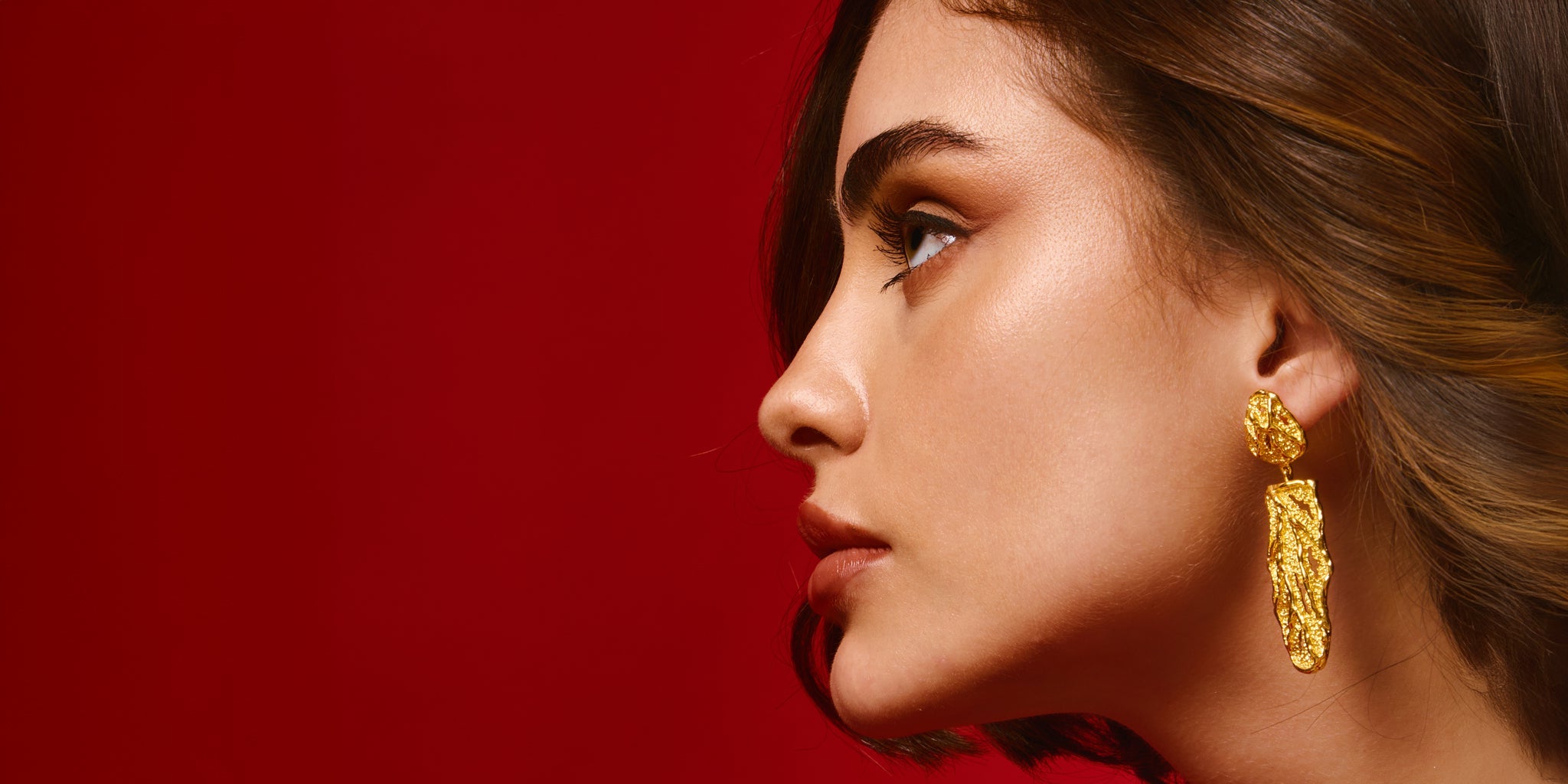 Woman wearing 22K gold plated  earrings against a red background