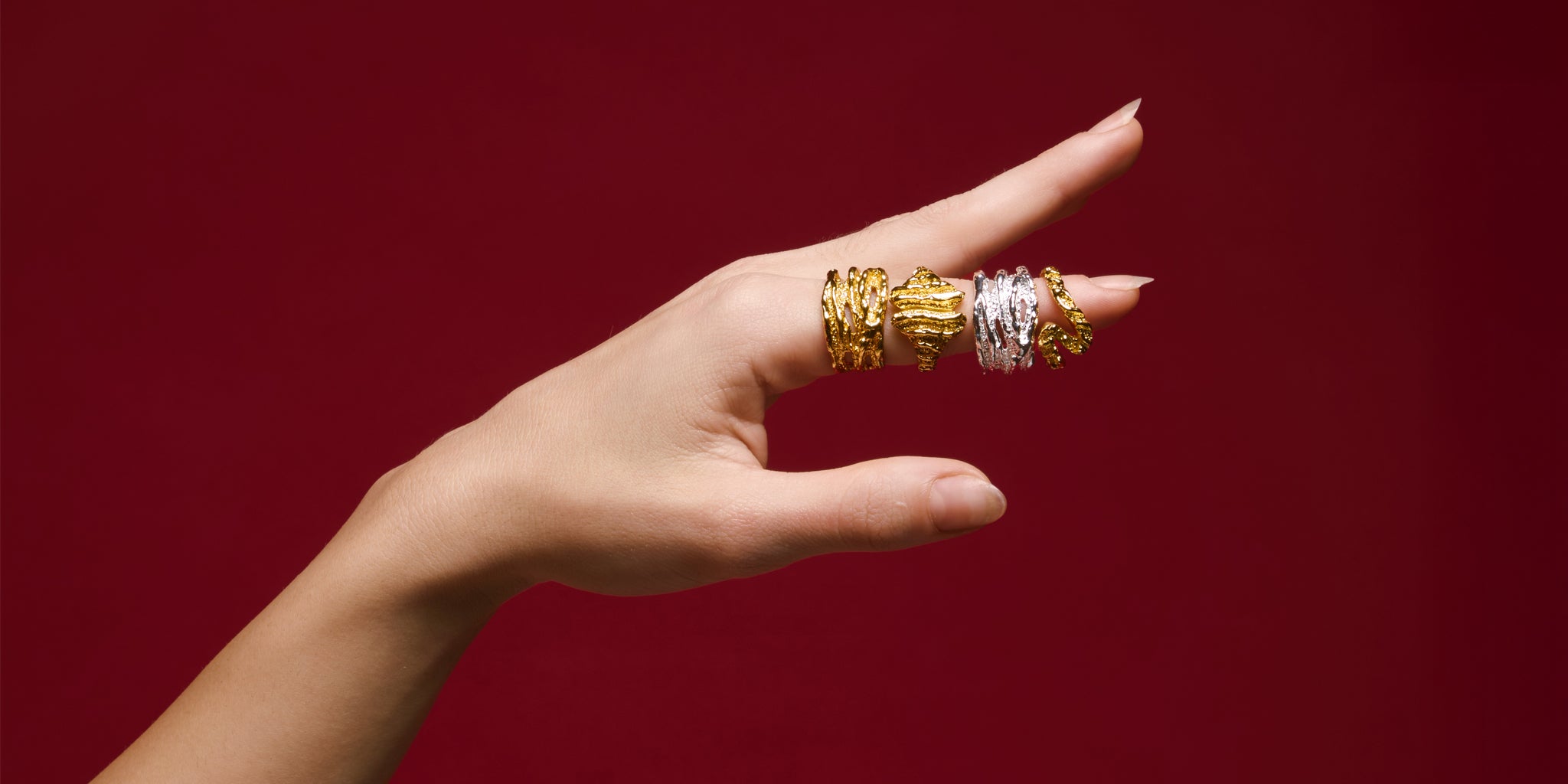 Hand wearing gold and silver rings with a red background