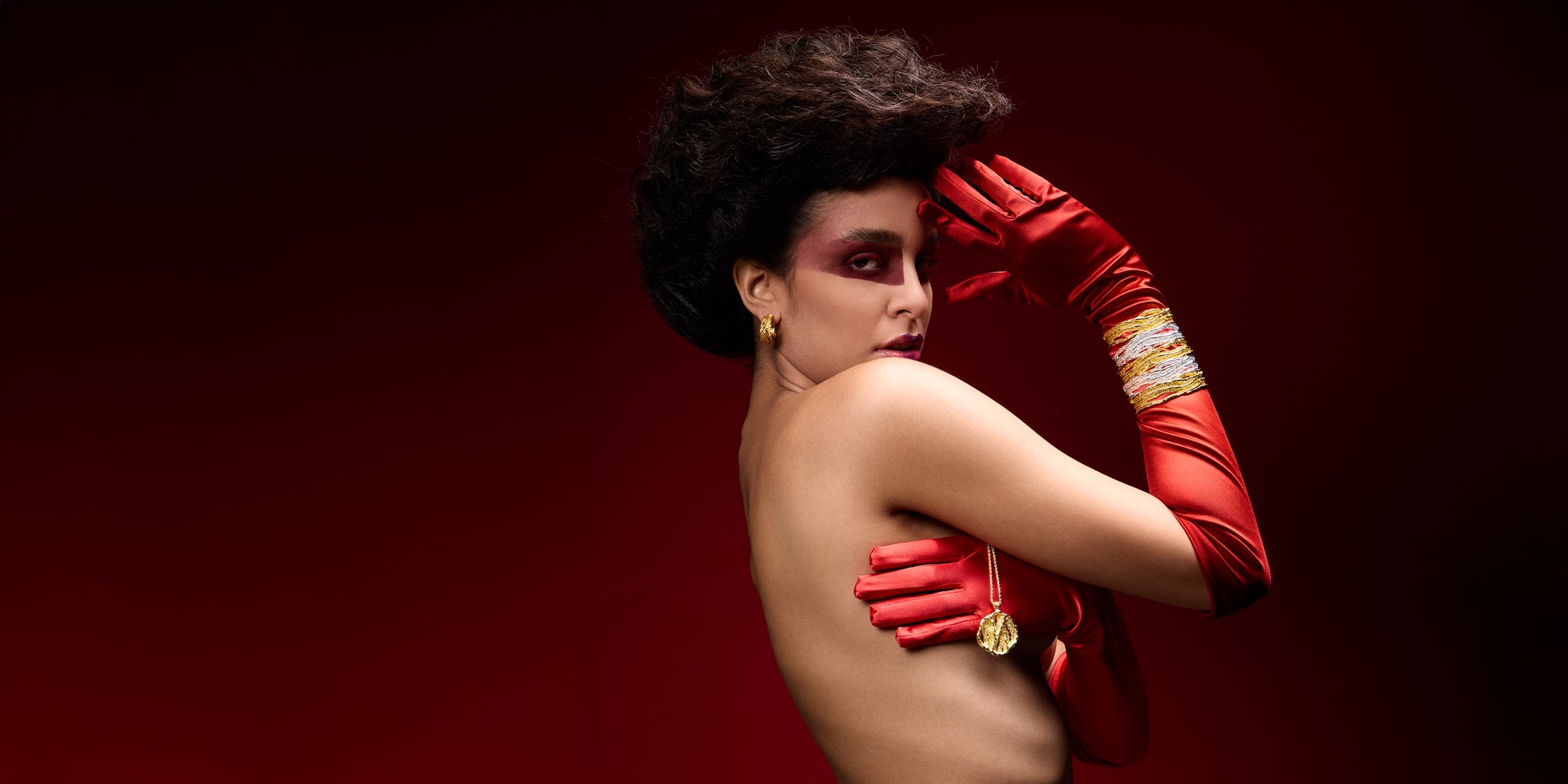 Woman wearing red gloves and a dark wig against a red background