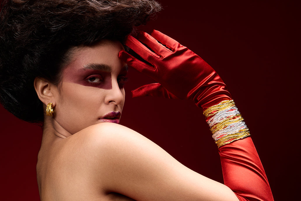 Woman wearing a red glove and gold bracelets on a dark red background