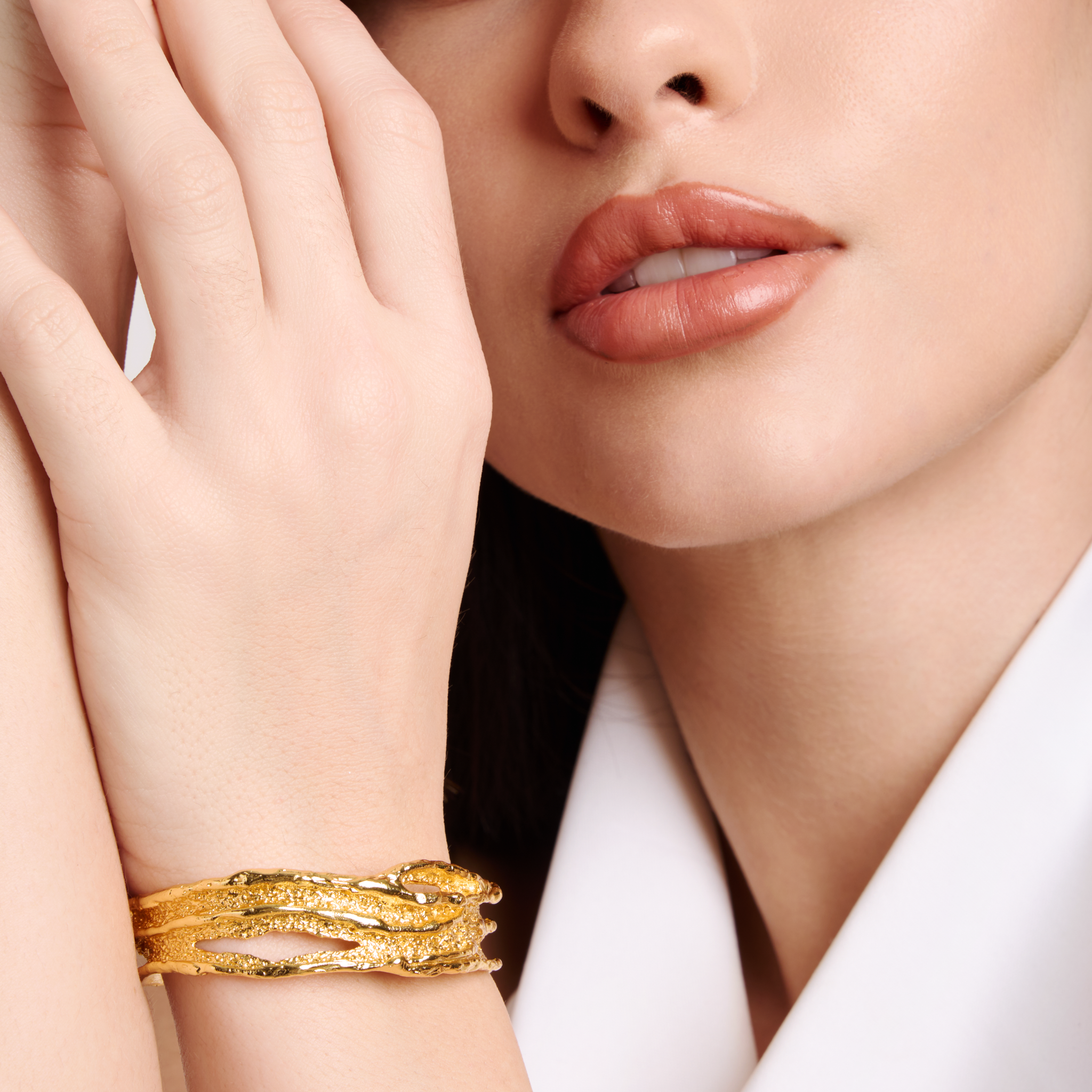 Close-up of a woman's face with a gold plated bracelet on her wrist