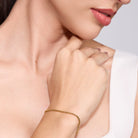 Close-up of a woman wearing a gold bracelet on a plain background
