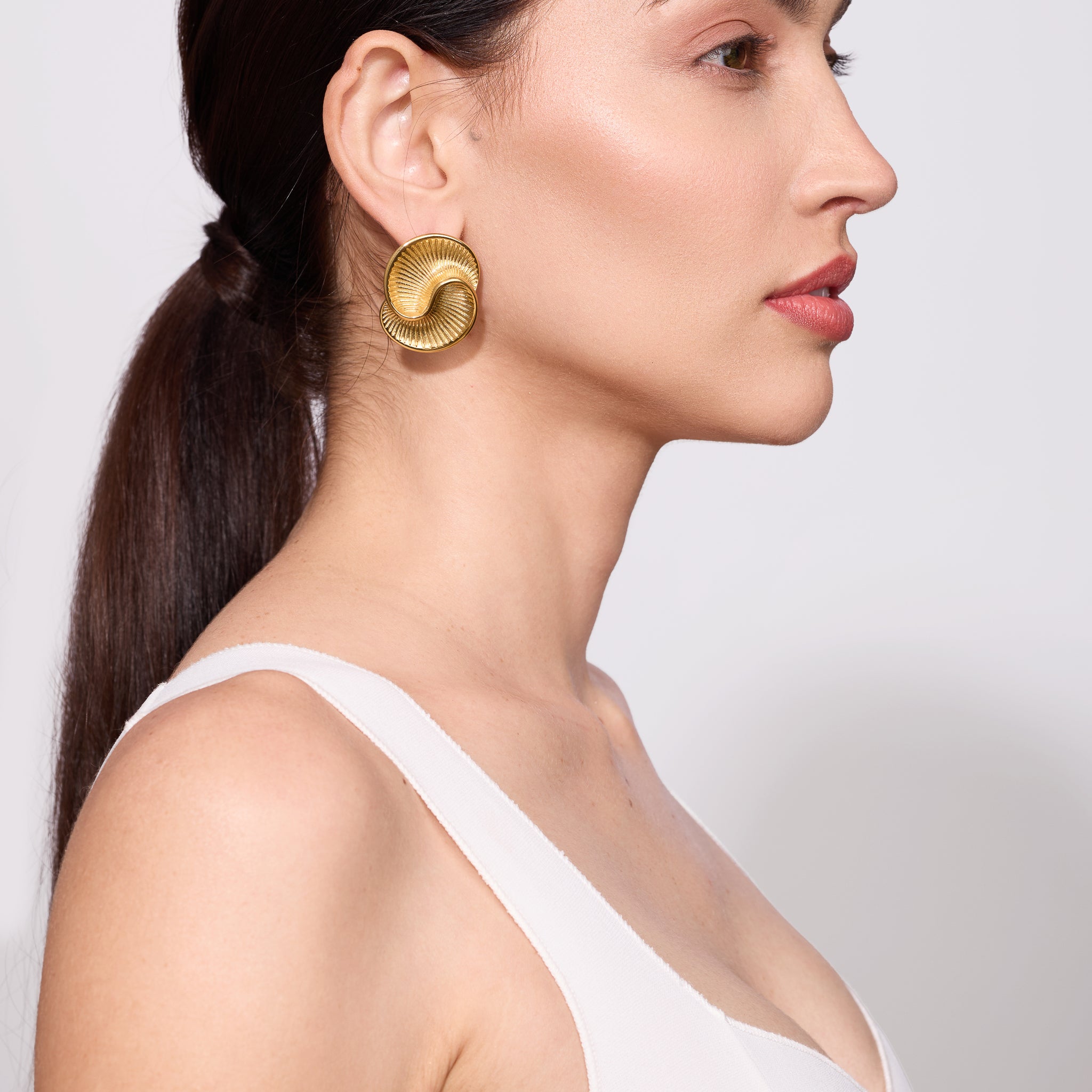 Woman wearing gold earrings with a plain background