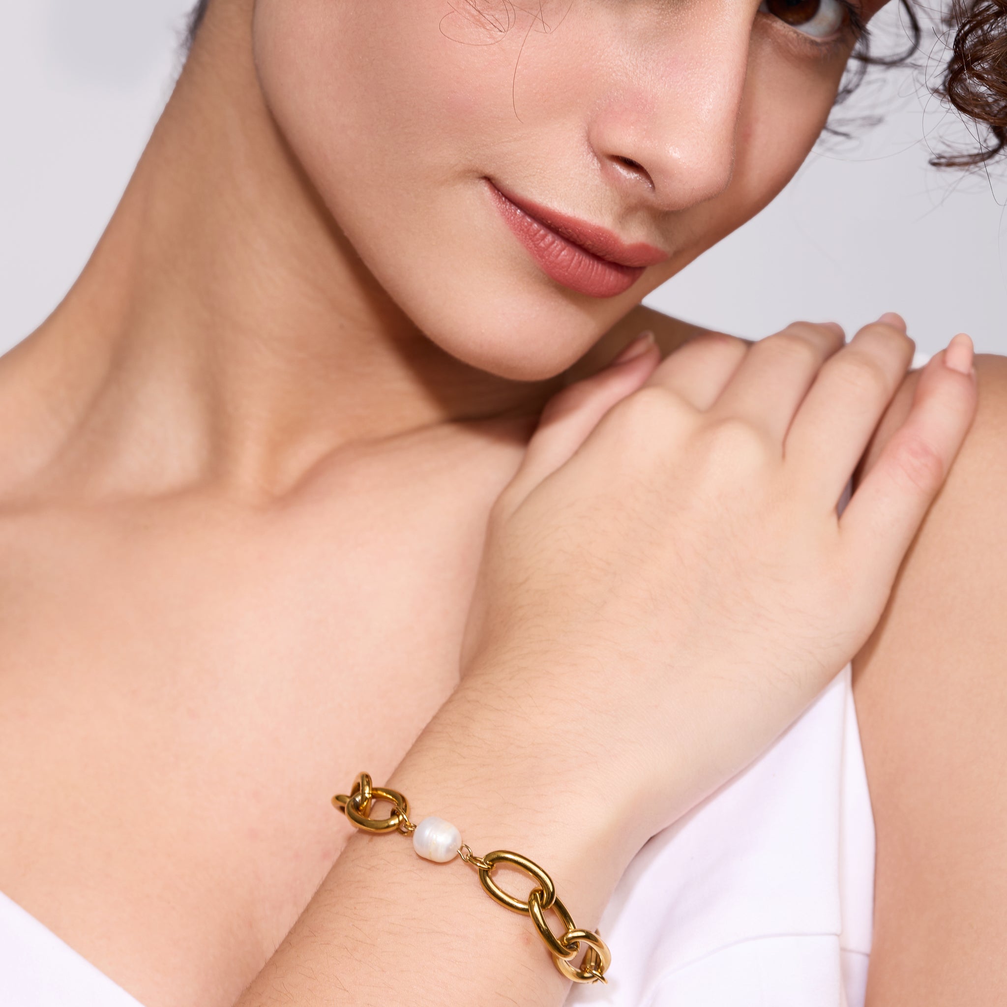 Woman wearing a gold bracelet with a pearl on a plain background