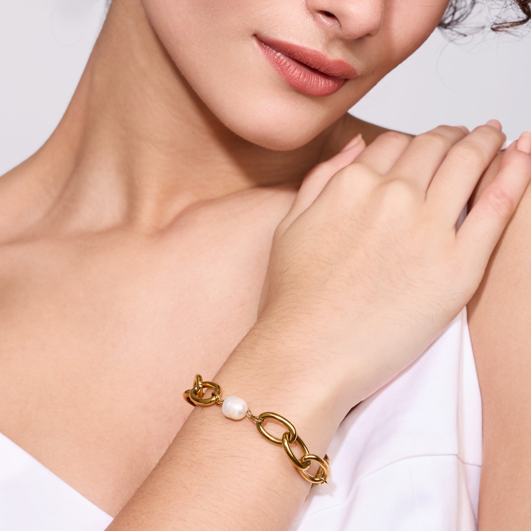 Gold bracelet with a pearl on a women's wrist against a white background