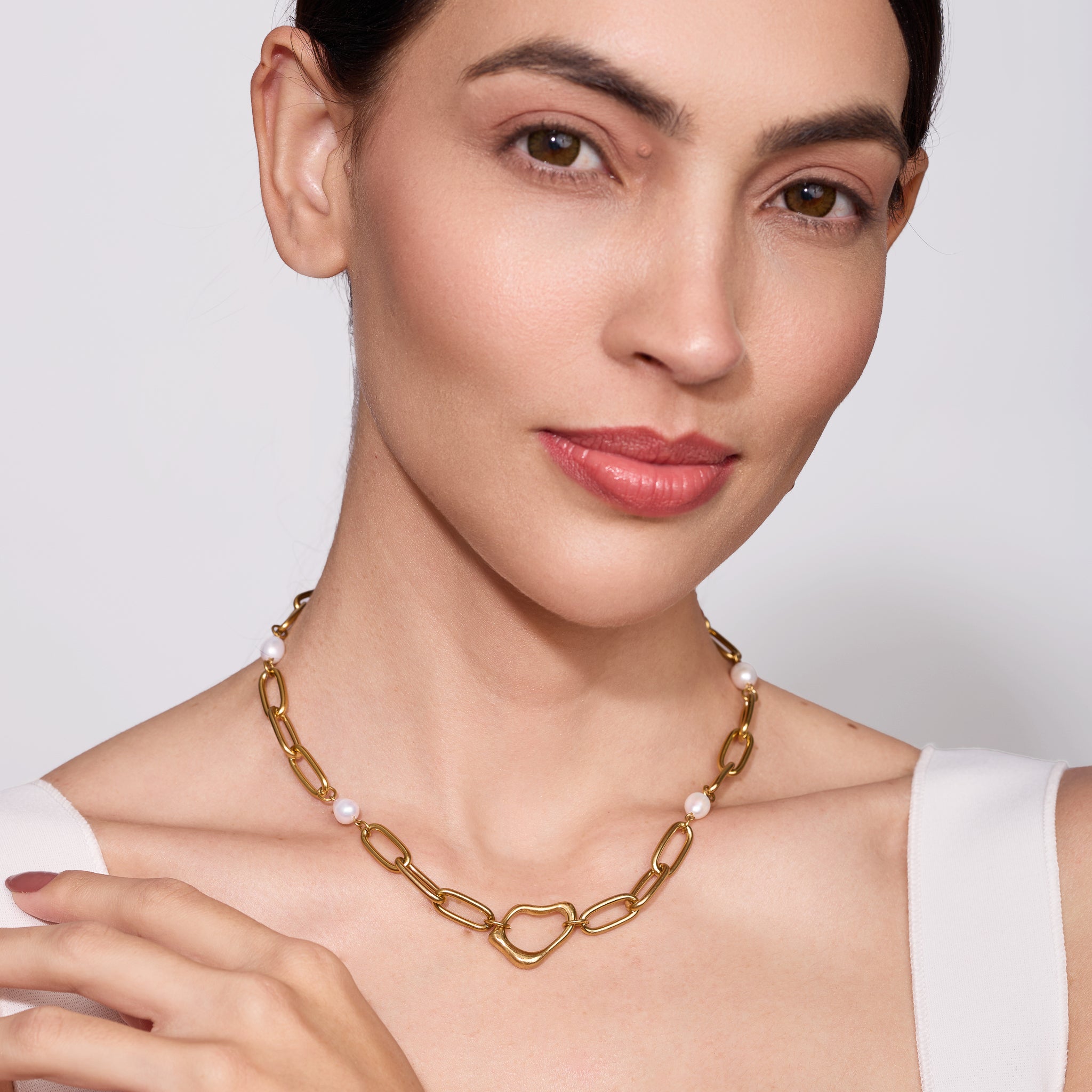 Woman wearing a gold chain necklace with abstract center on a plain background