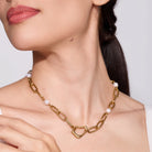 Woman wearing a gold chain necklace with abstract center on a plain background