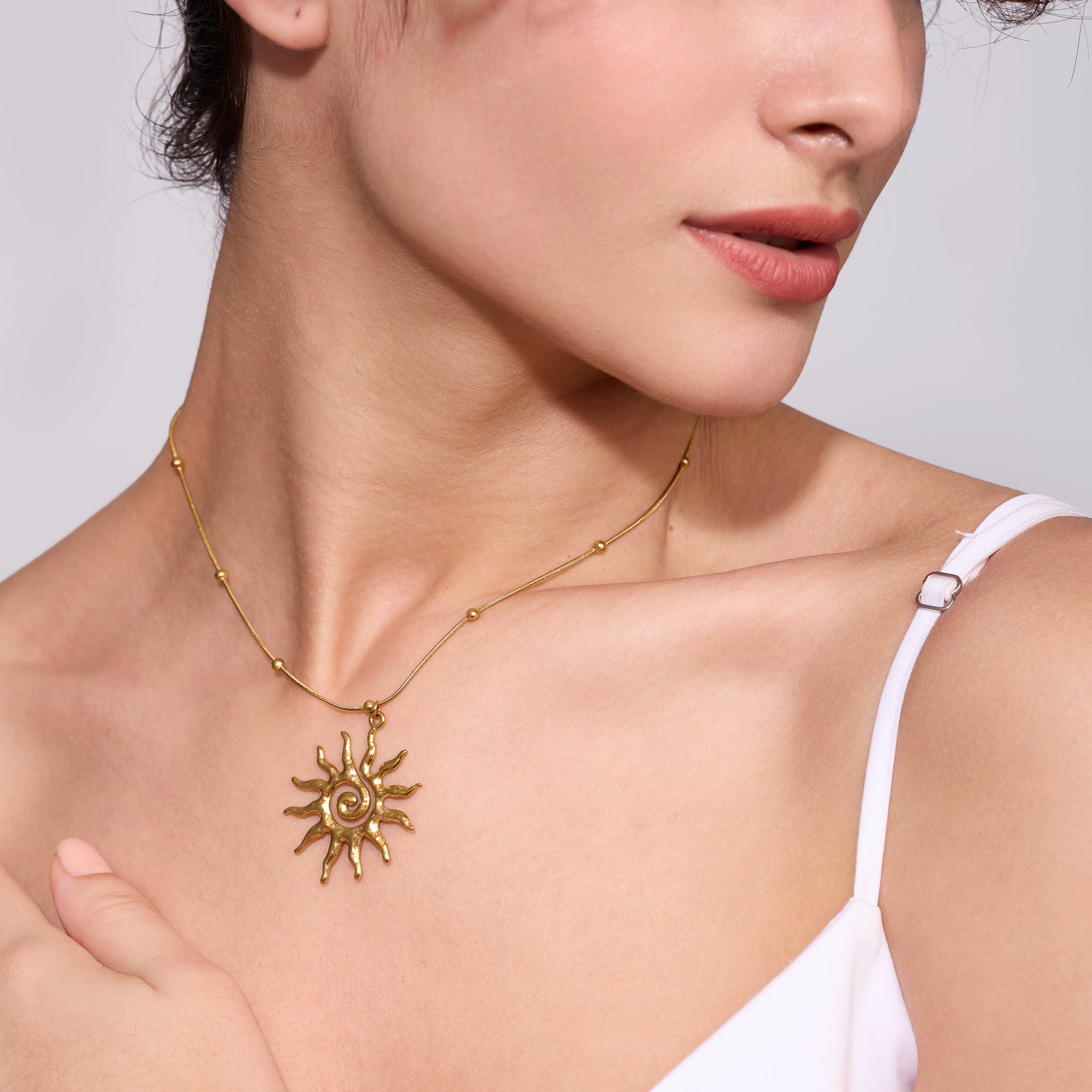 Gold necklace with a sun pendant worn by a model against a neutral background