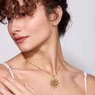 Woman wearing a gold necklace with a sun pendant on a plain background