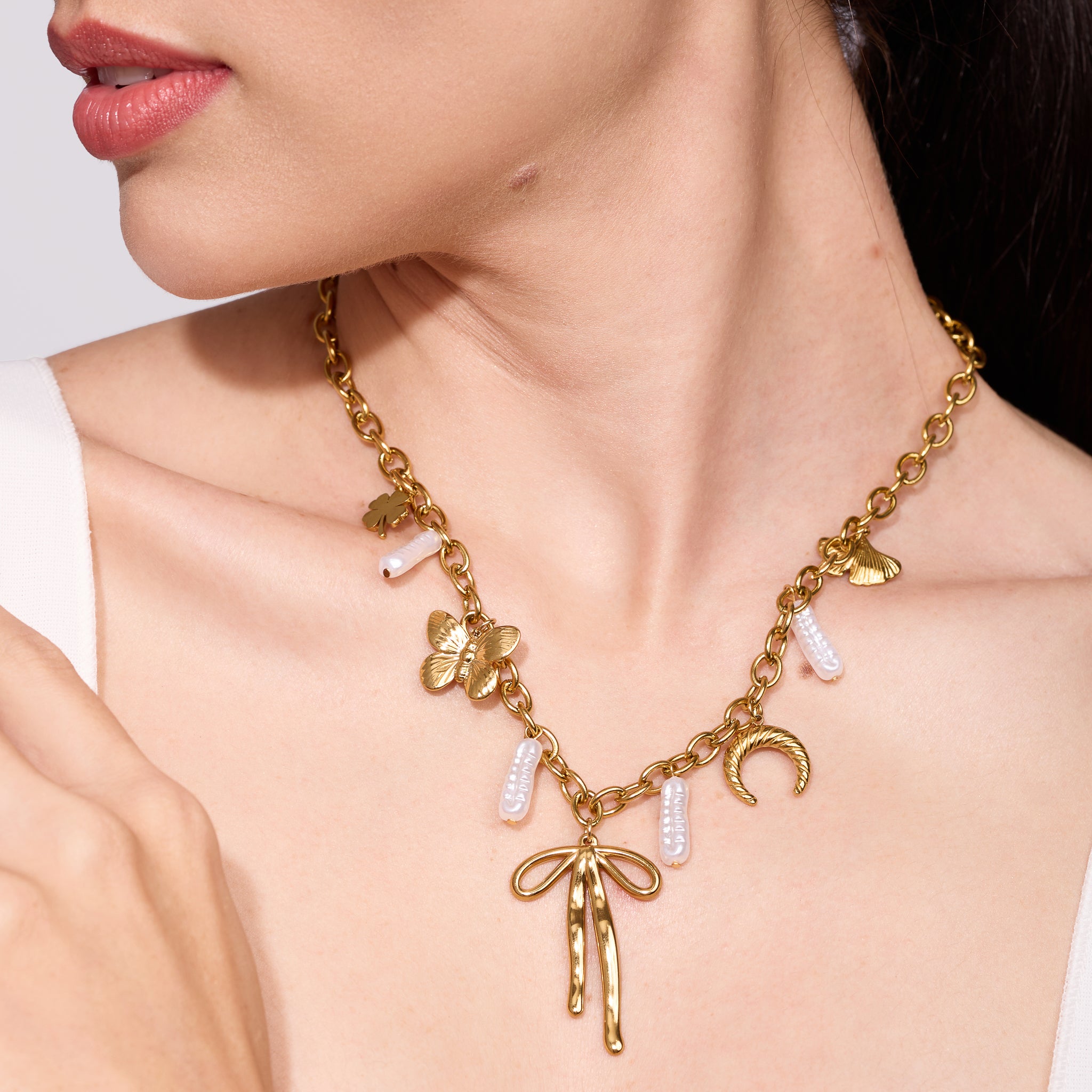 Gold necklace with ribbon charms worn by women on a neutral background