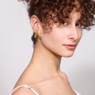 Woman wearing 18K gold plated earrings against a plain background