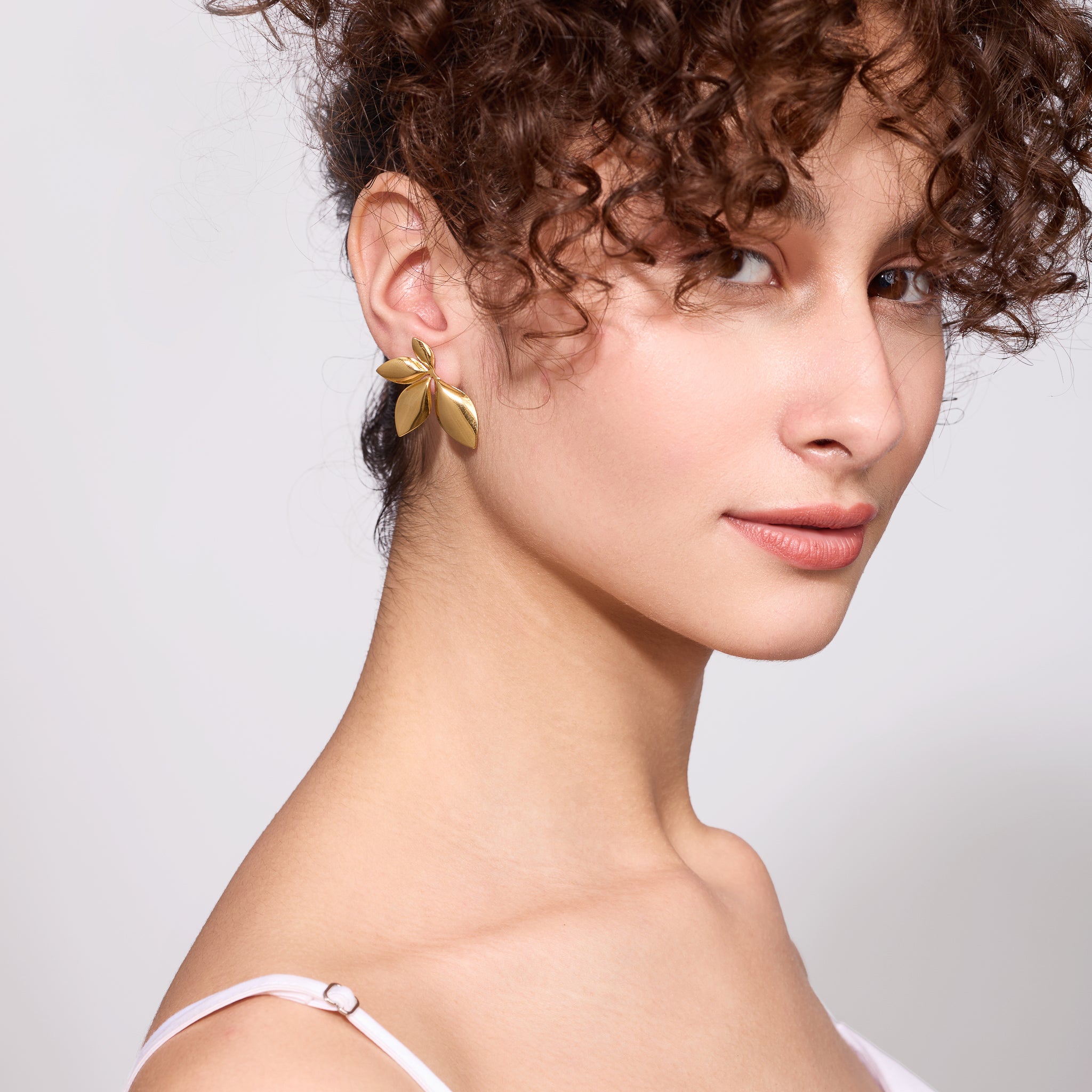 Woman wearing 18K gold plated earrings against a plain background