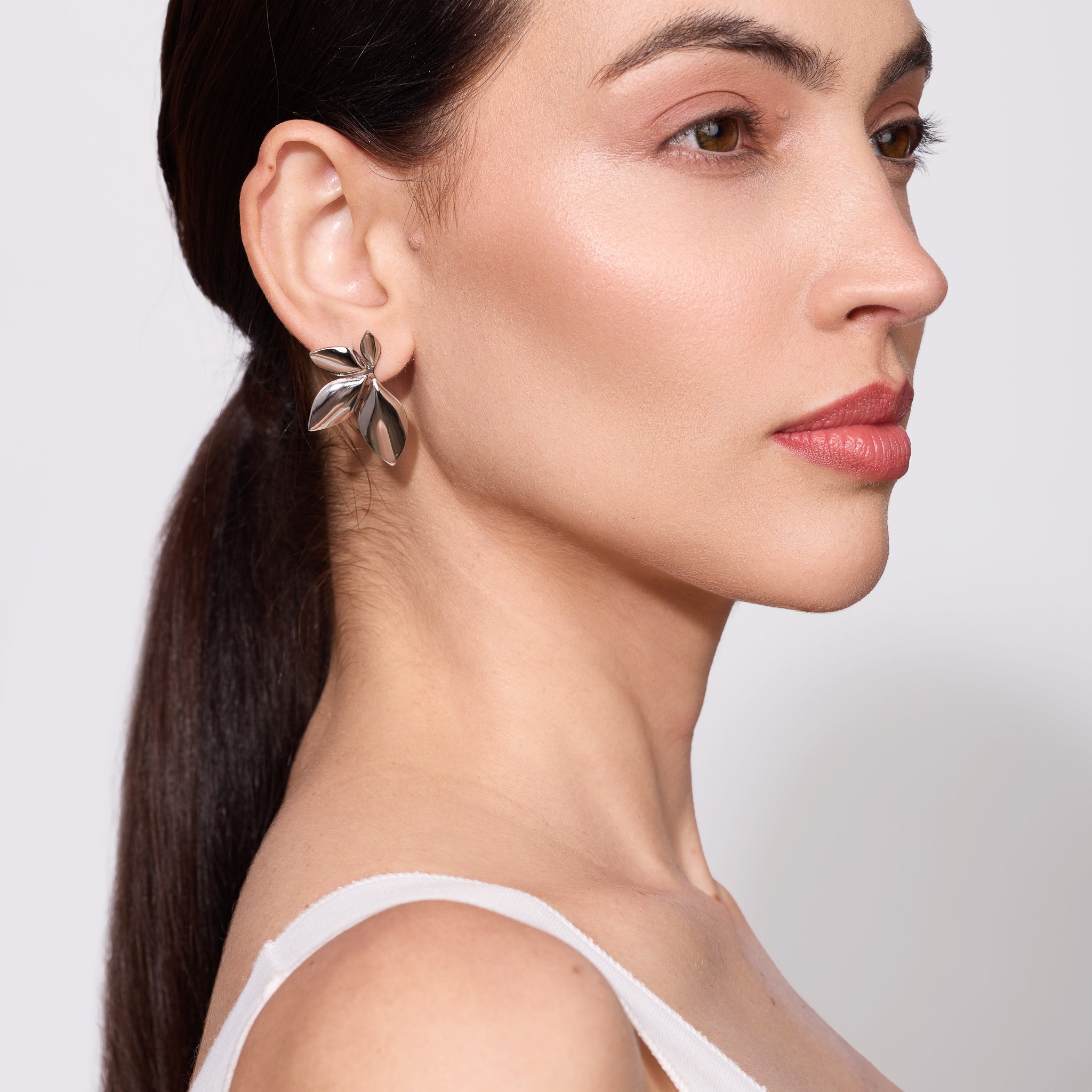 Close-up of a woman wearing a silver plated leaf-shaped earring against a neutral background