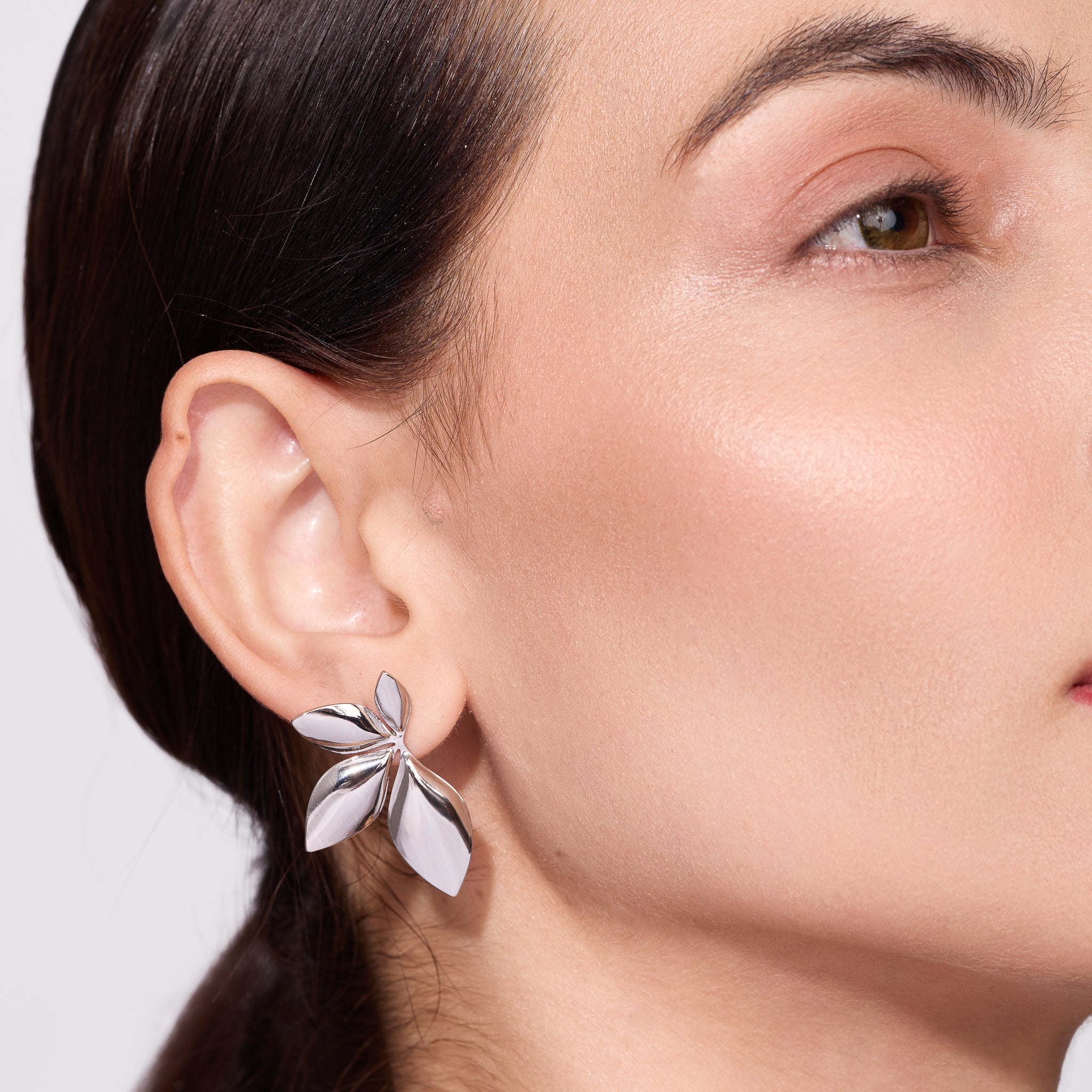 Silver plated leaf earring worn by a person on a neutral background