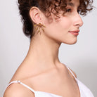 Close-up of a woman wearing gold arrow shaped earrings with a plain background