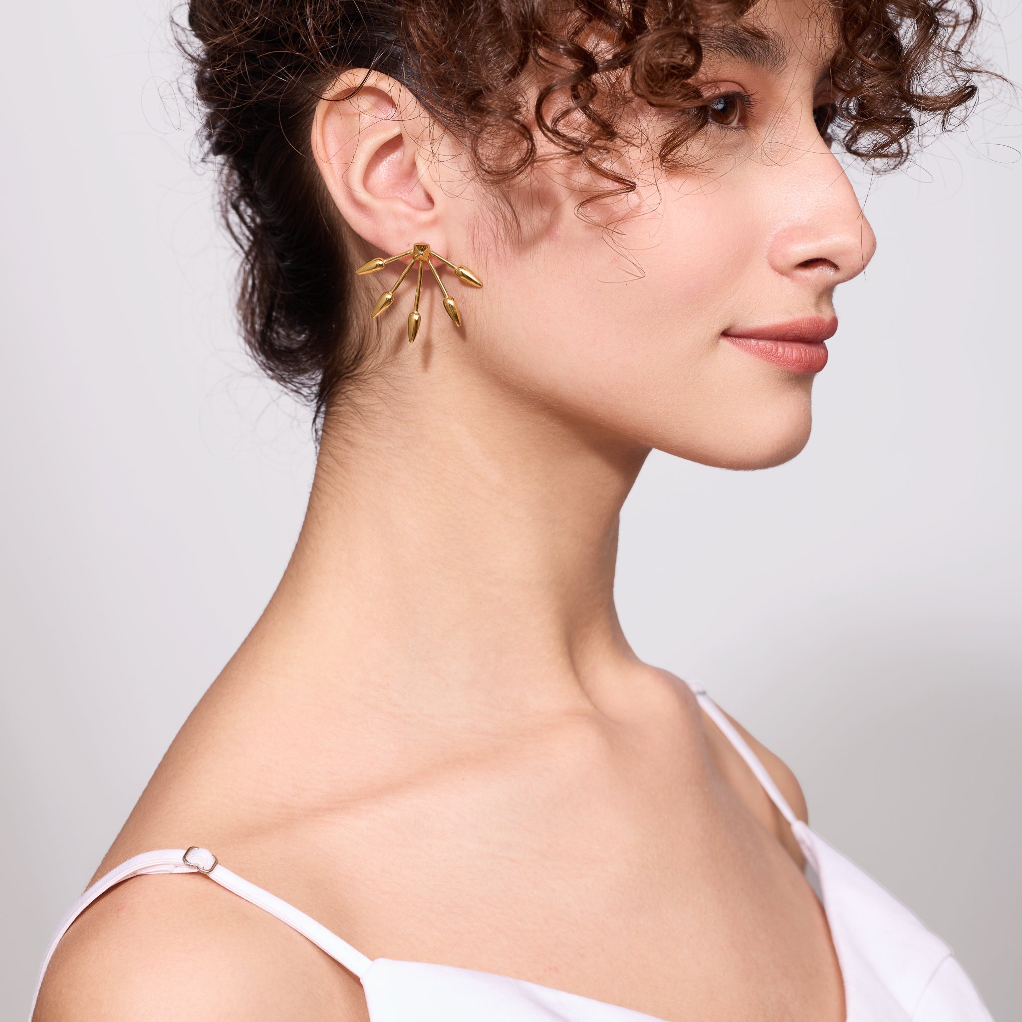 Close-up of a woman wearing gold arrow shaped earrings with a plain background