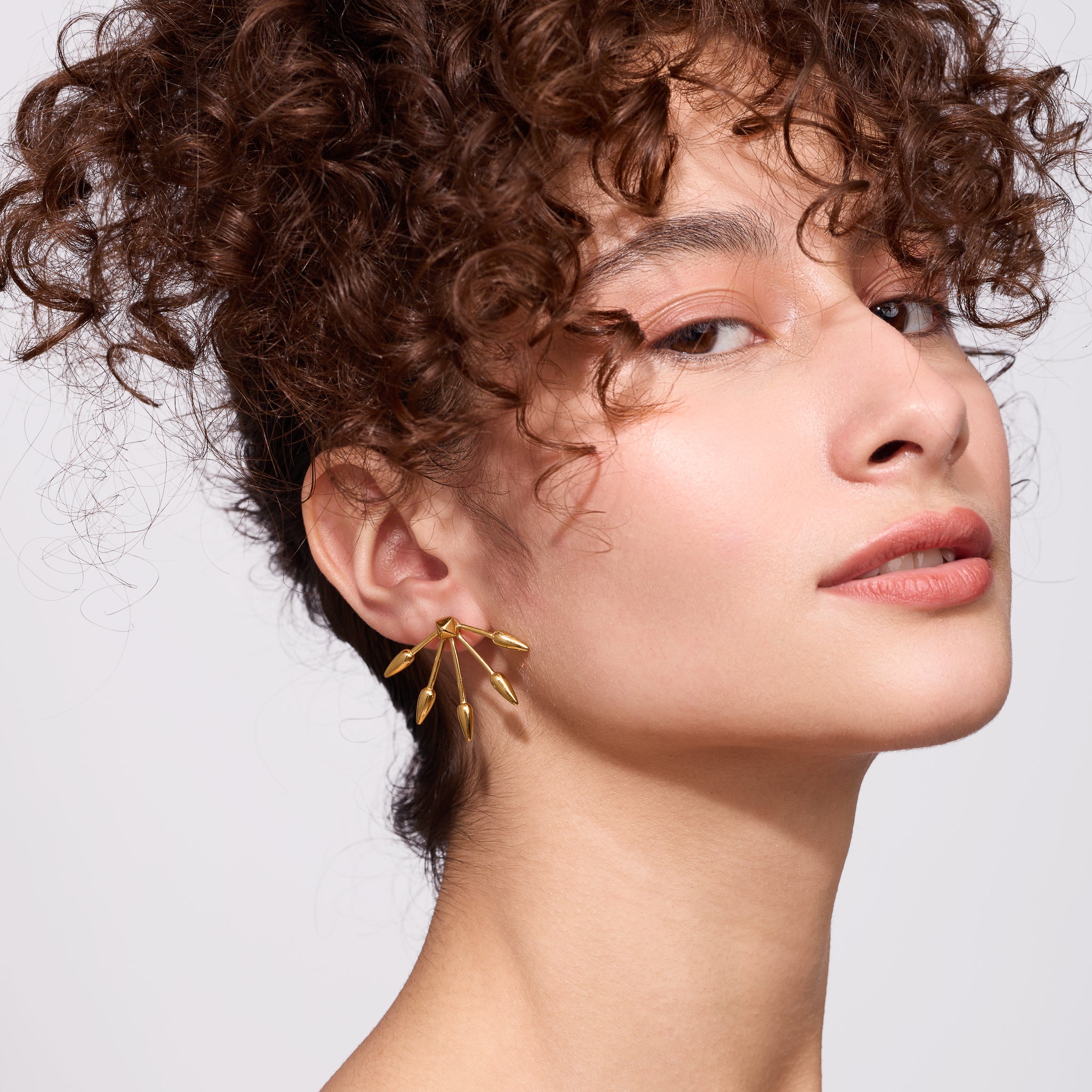 Close-up of a woman wearing gold arrow shaped earrings with a plain background