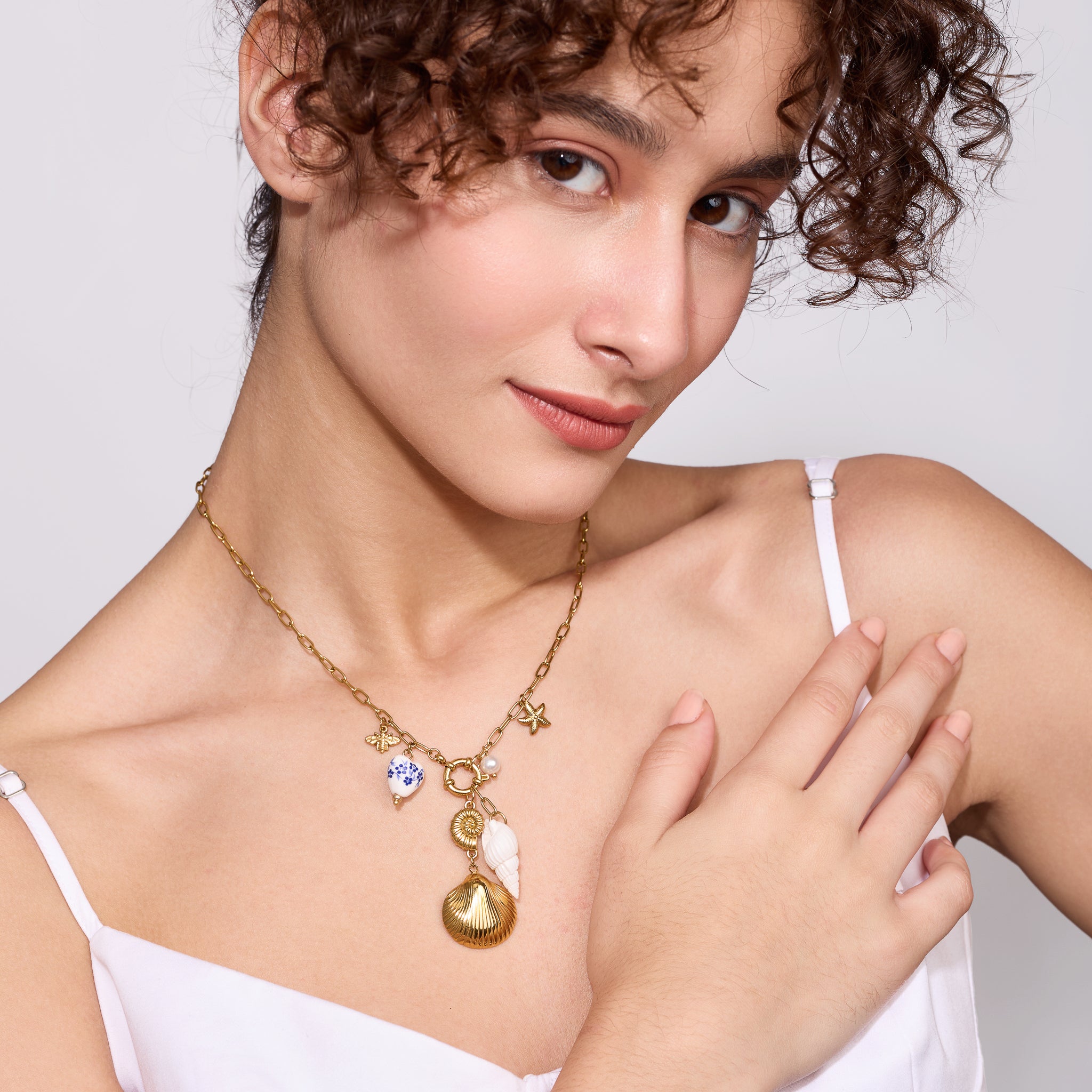 Woman wearing a gold necklace with charms on a plain background
