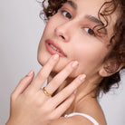Woman with a gold ring on her finger against a neutral background
