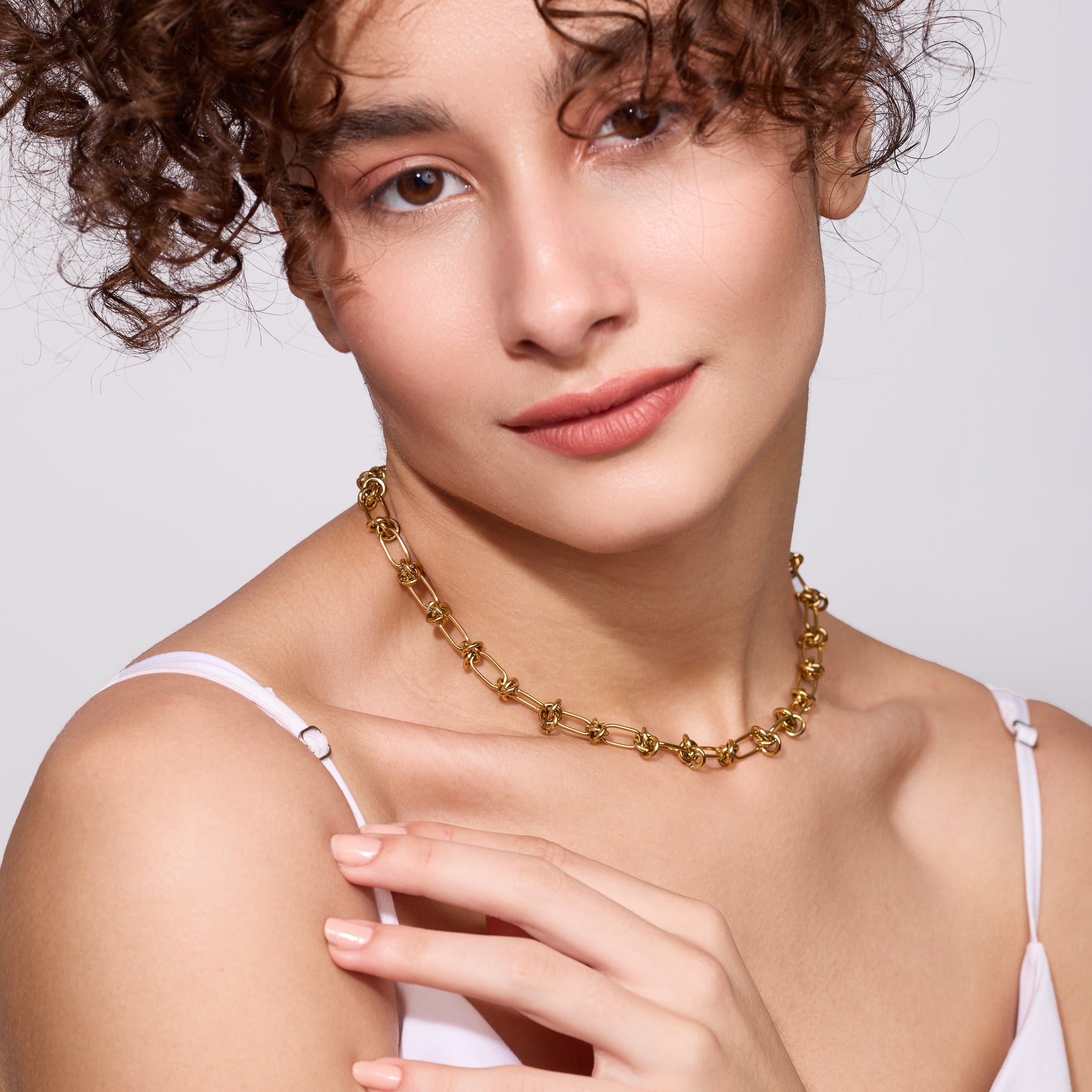 Woman wearing a gold necklace against a plain background