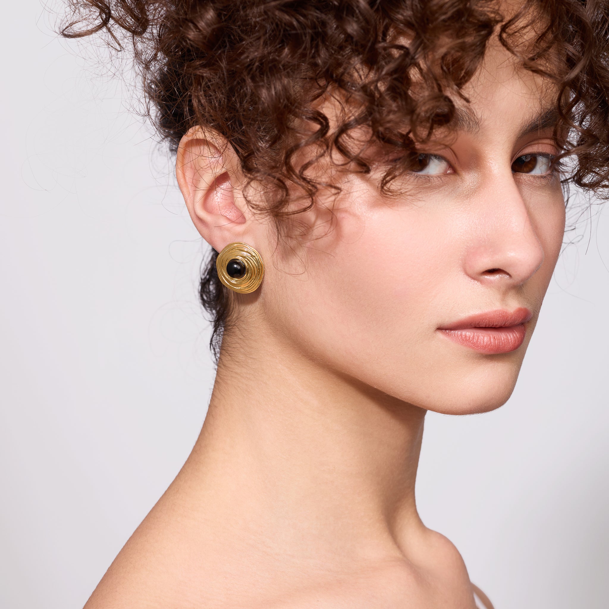 Close-up of a woman wearing gold earrings against a neutral background