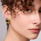 Close-up of a woman wearing gold earrings with a gray background