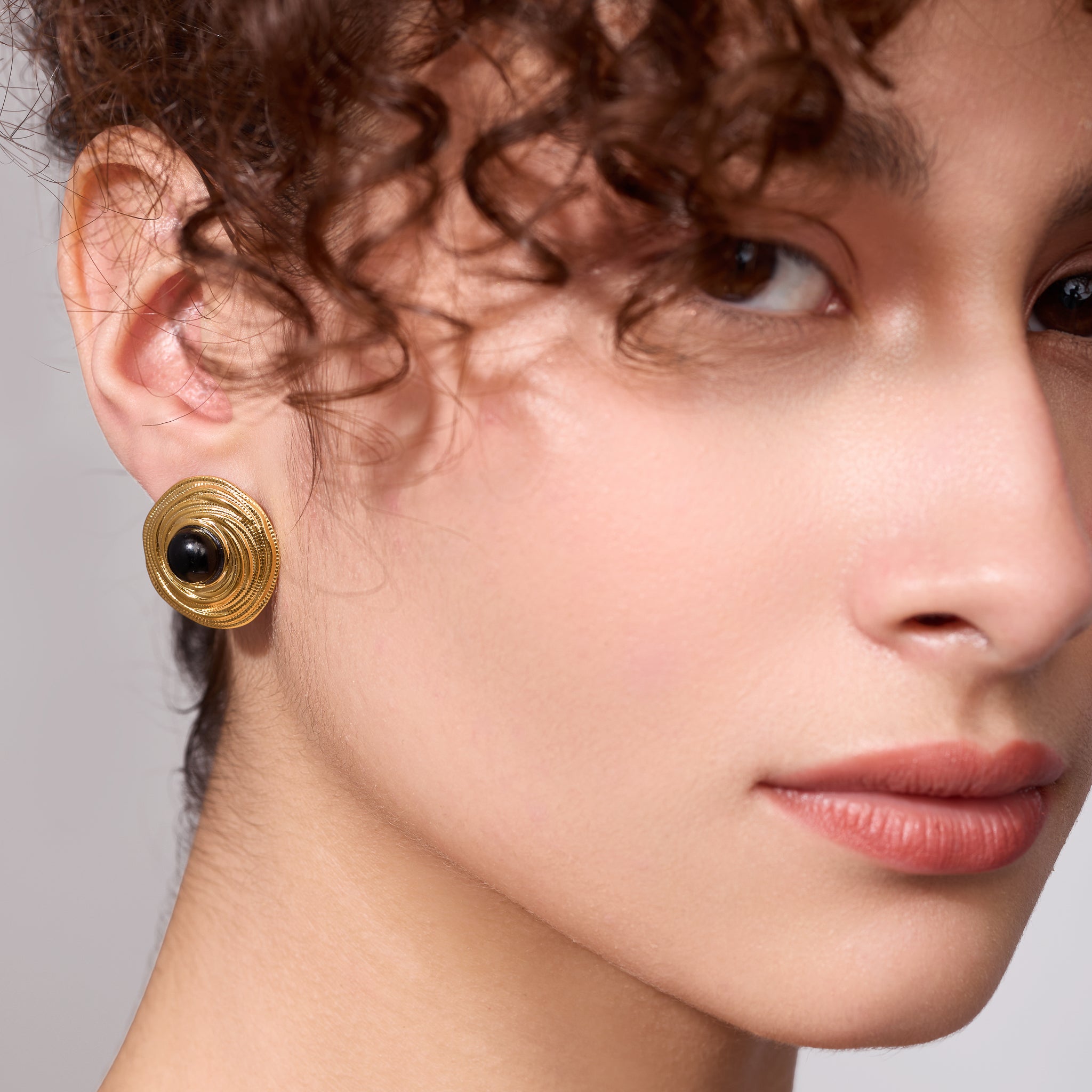 Close-up of a woman wearing gold earrings with a gray background