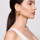 Woman wearing gold hoop earrings with a plain background