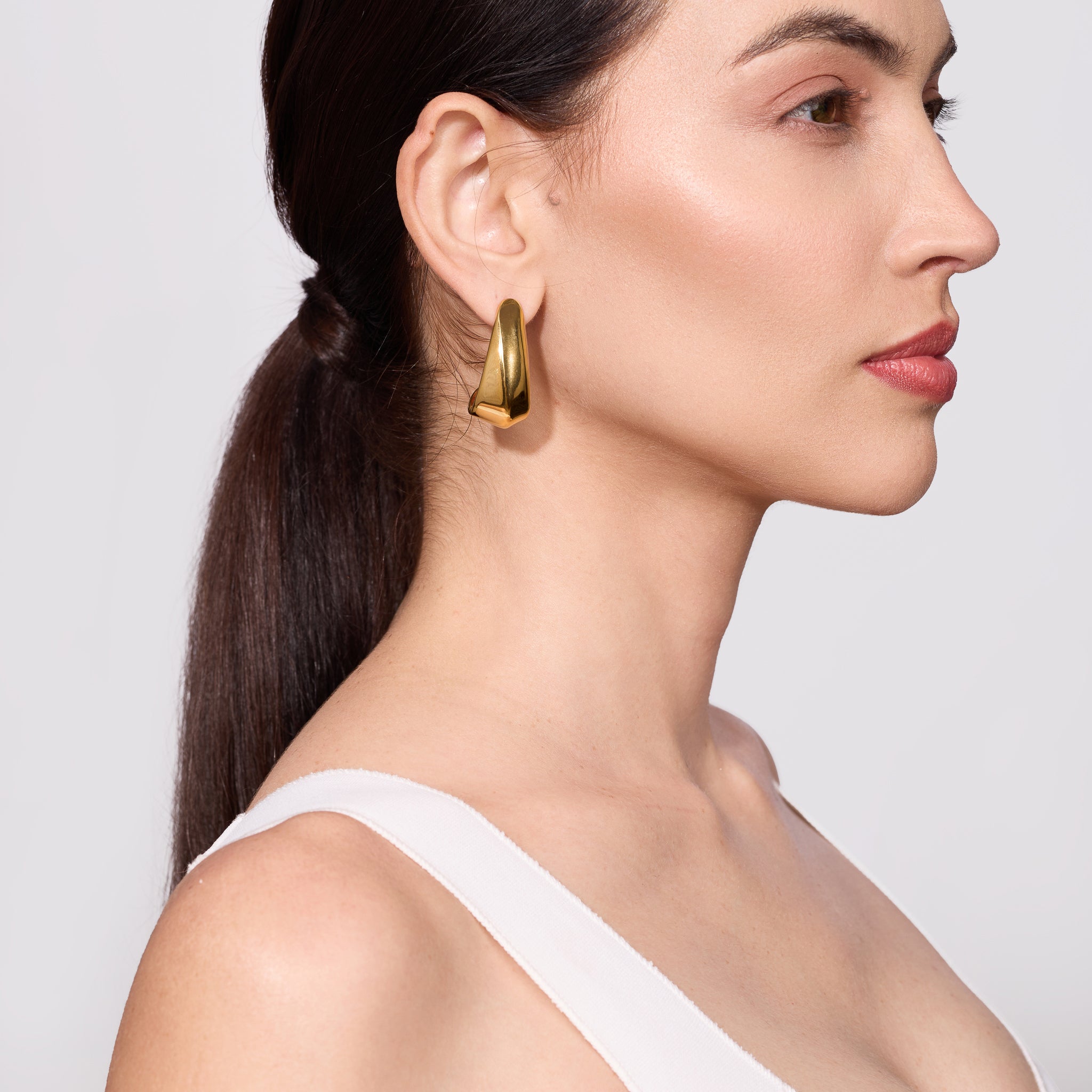 Woman wearing gold hoop earrings with a plain background