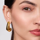 Close-up of a woman wearing a gold hoop earring against a neutral background