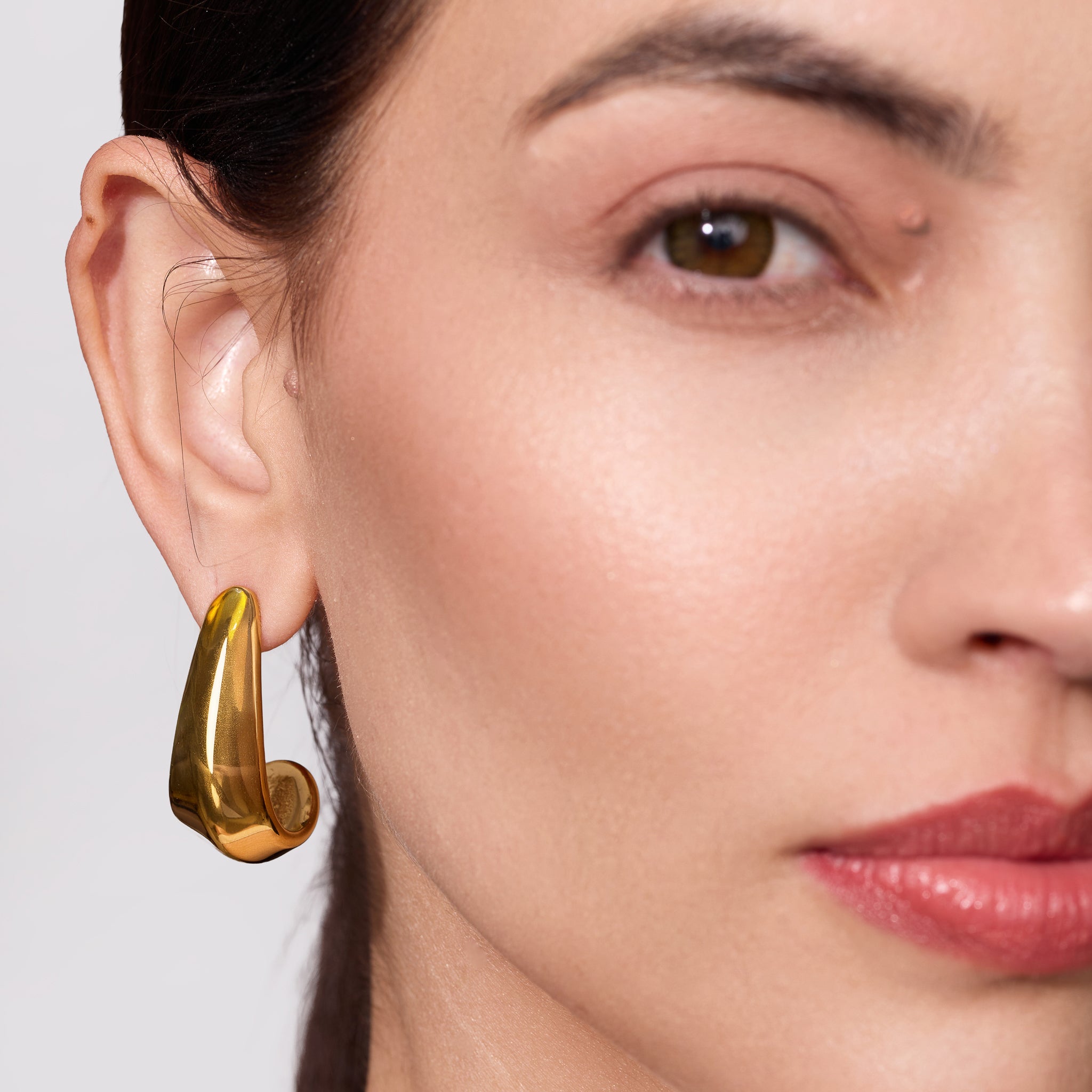 Close-up of a woman wearing a gold hoop earring against a neutral background