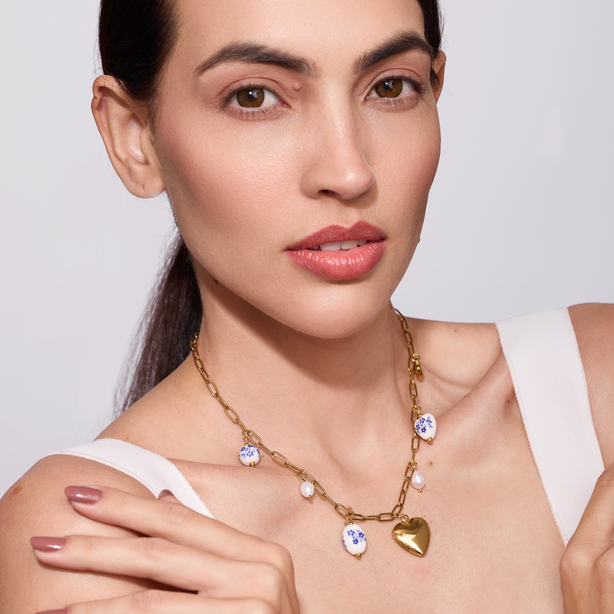 Woman wearing a gold necklace with heart and round pendants on a plain background