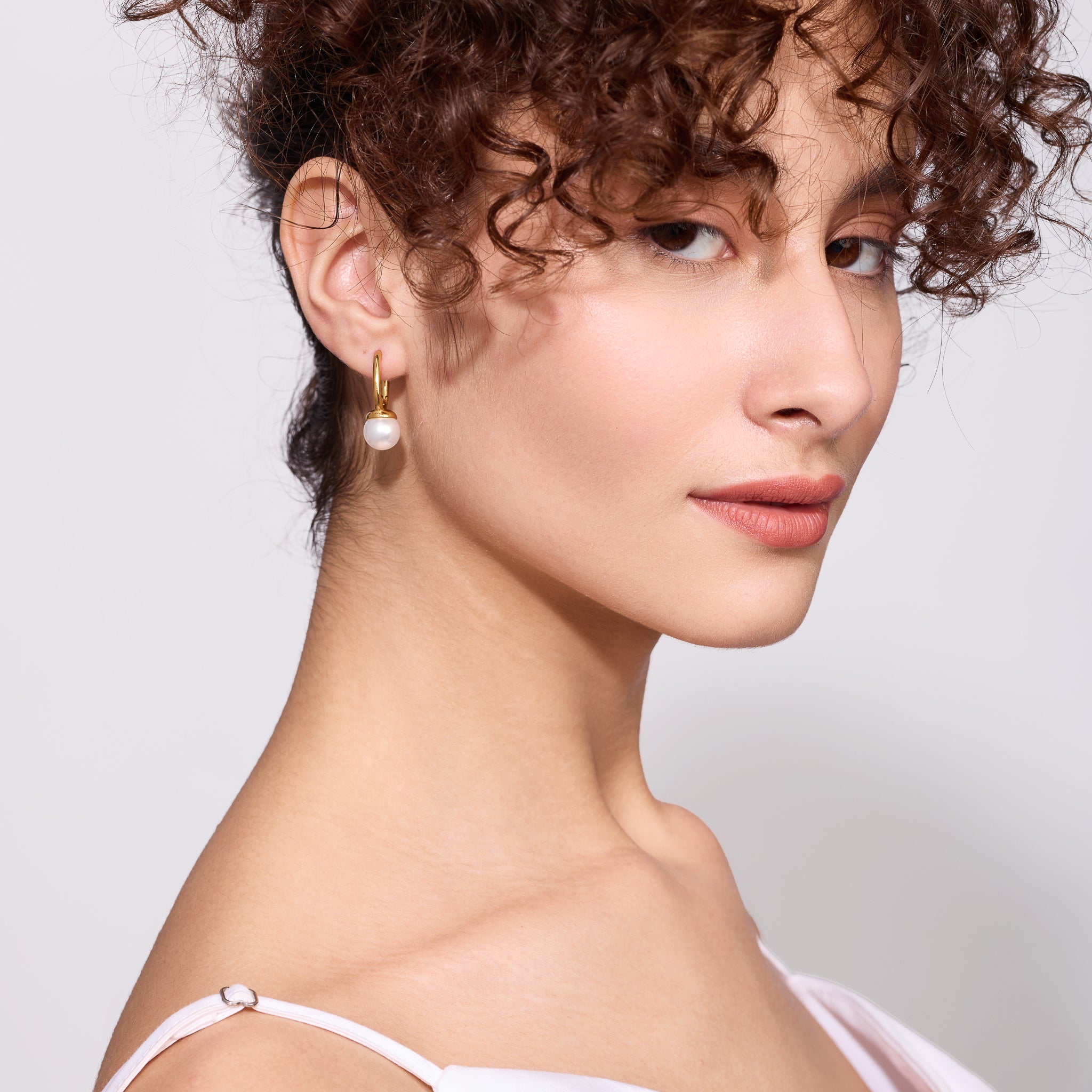 Close-up of a woman wearing pearl earrings against a neutral background