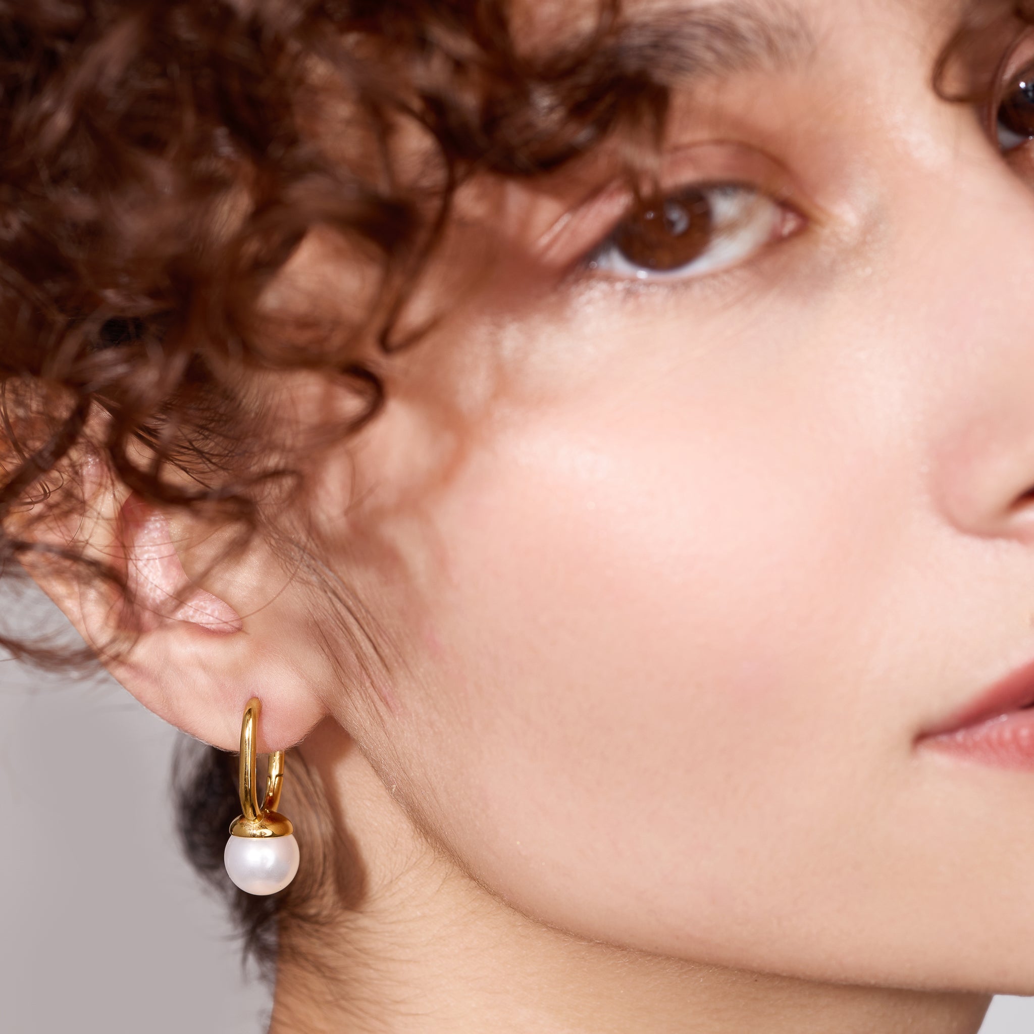 Close-up of a person wearing a gold earring with a pearl detail.
