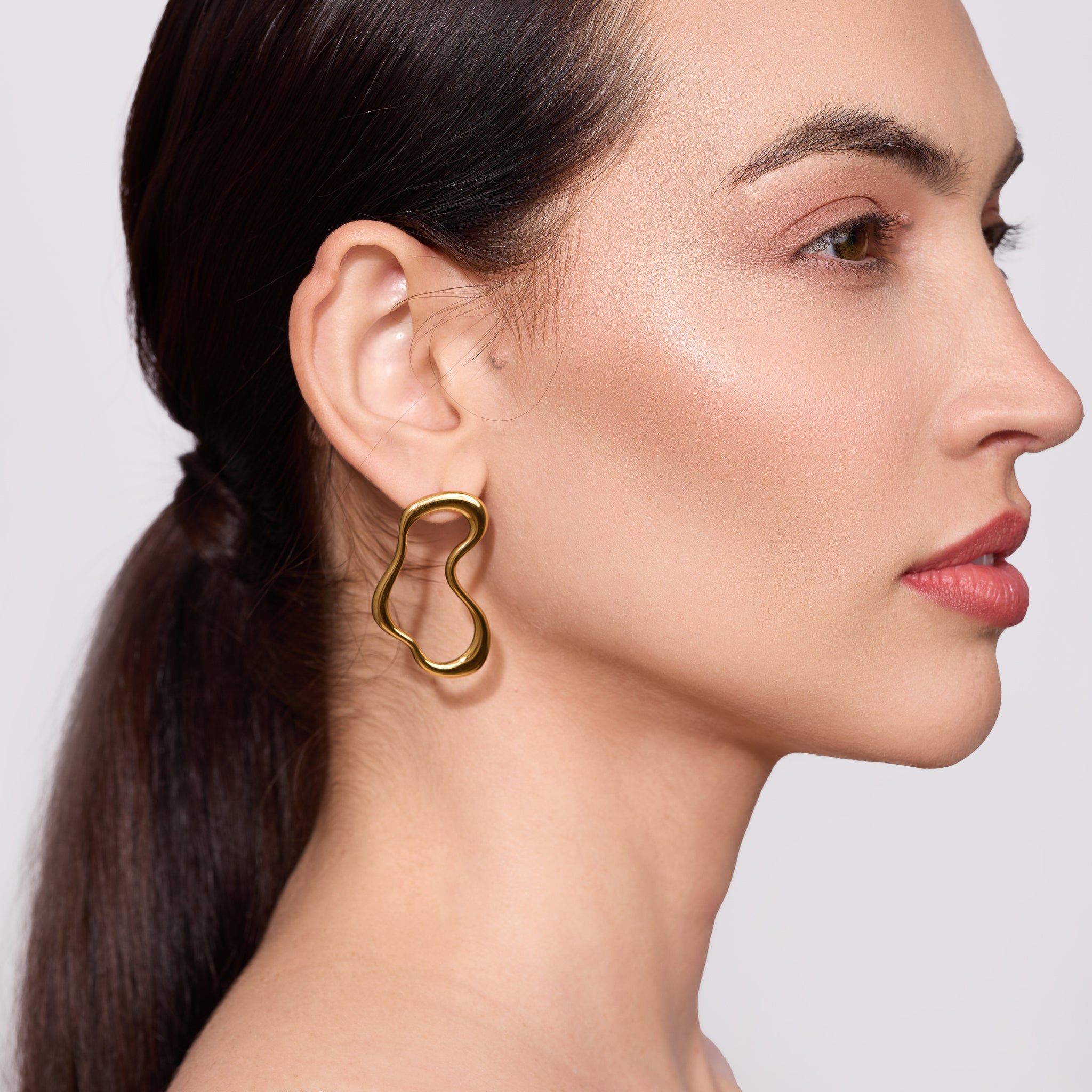 Close-up of a woman wearing a gold earring against a neutral background