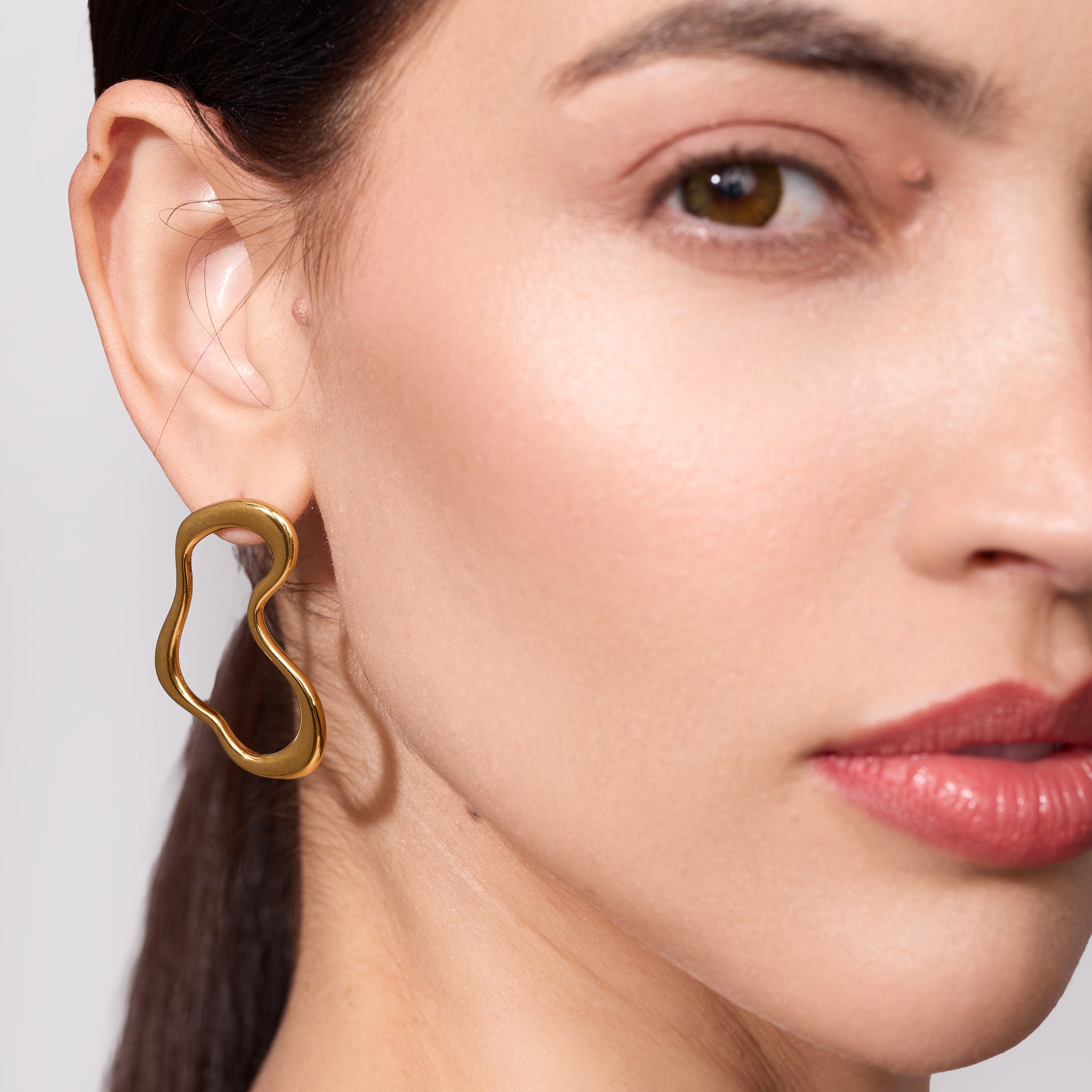 Close-up of a woman wearing a gold earring against a neutral background