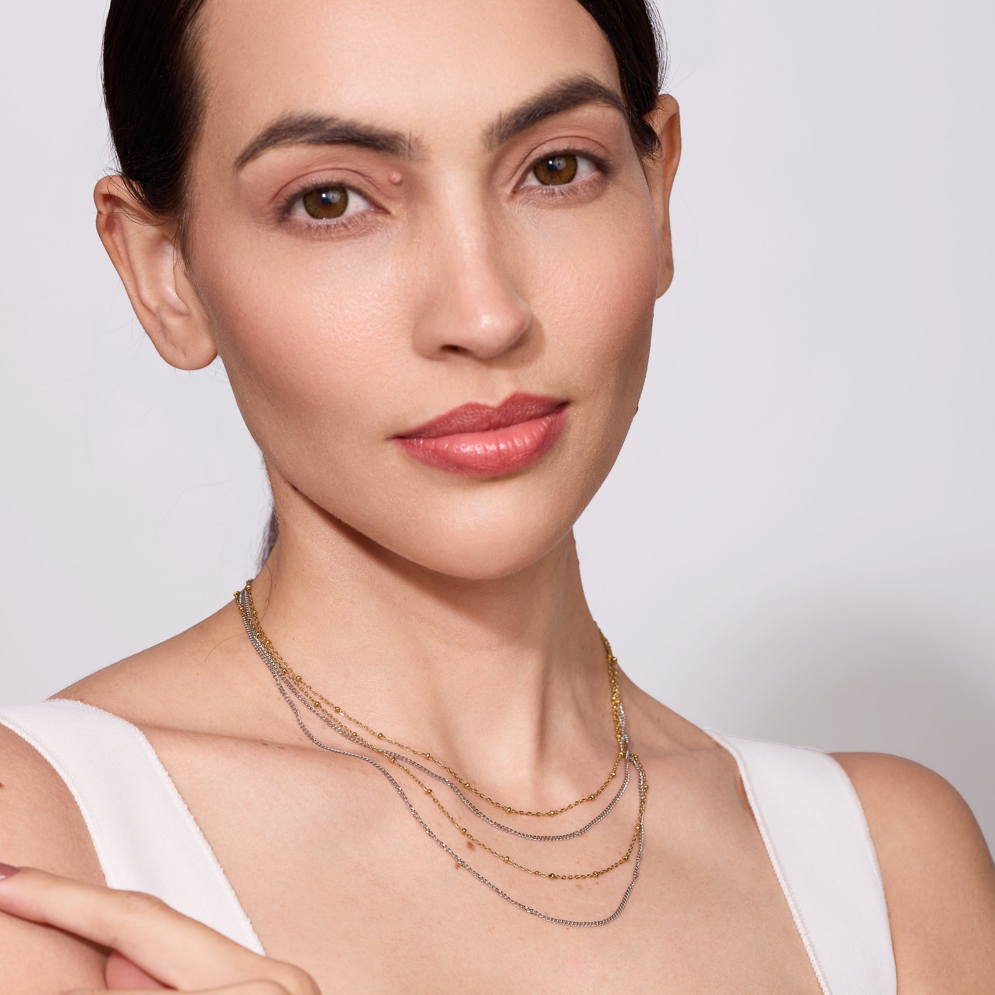 Woman wearing a three layer gold necklace against a plain background