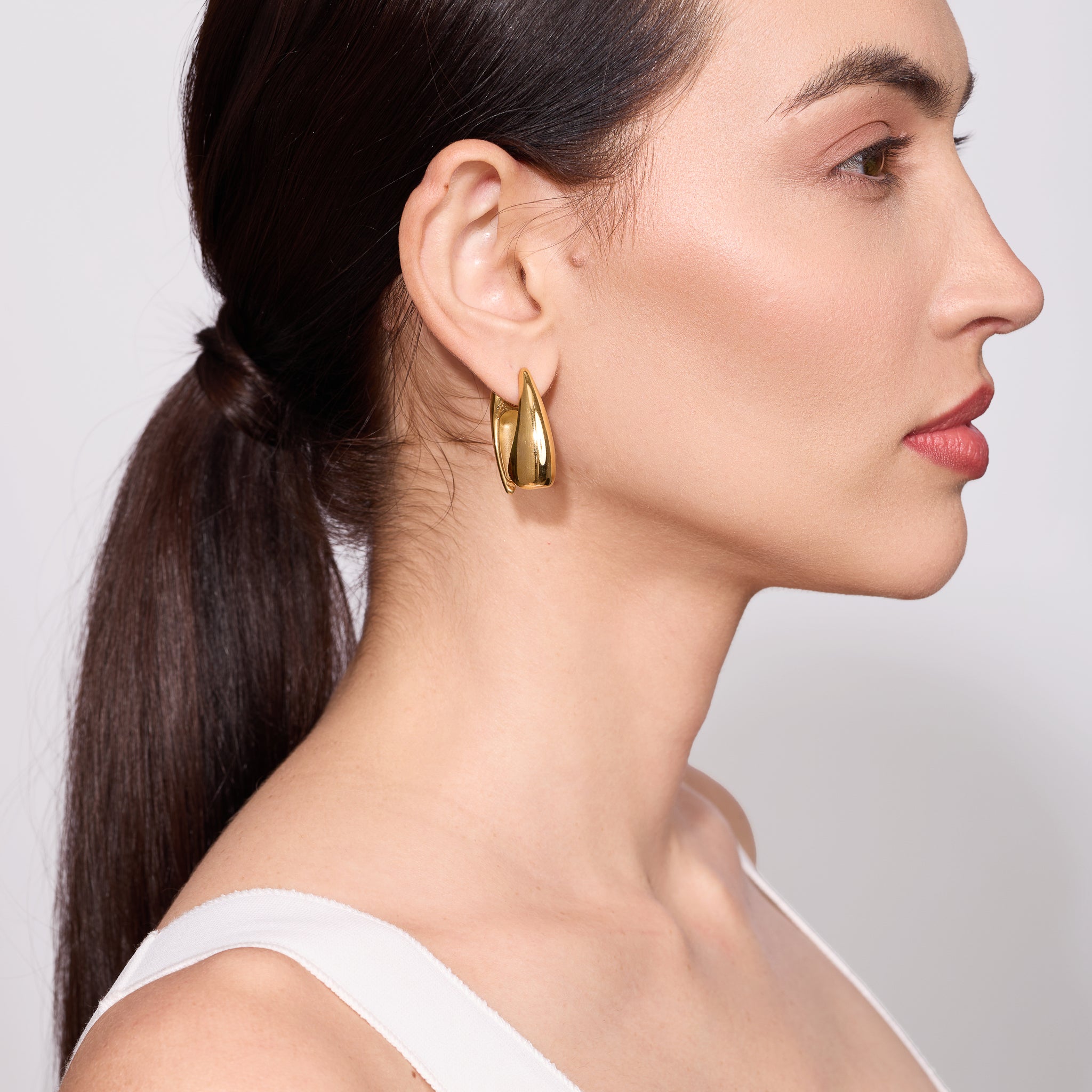 Woman wearing gold earrings with a plain background