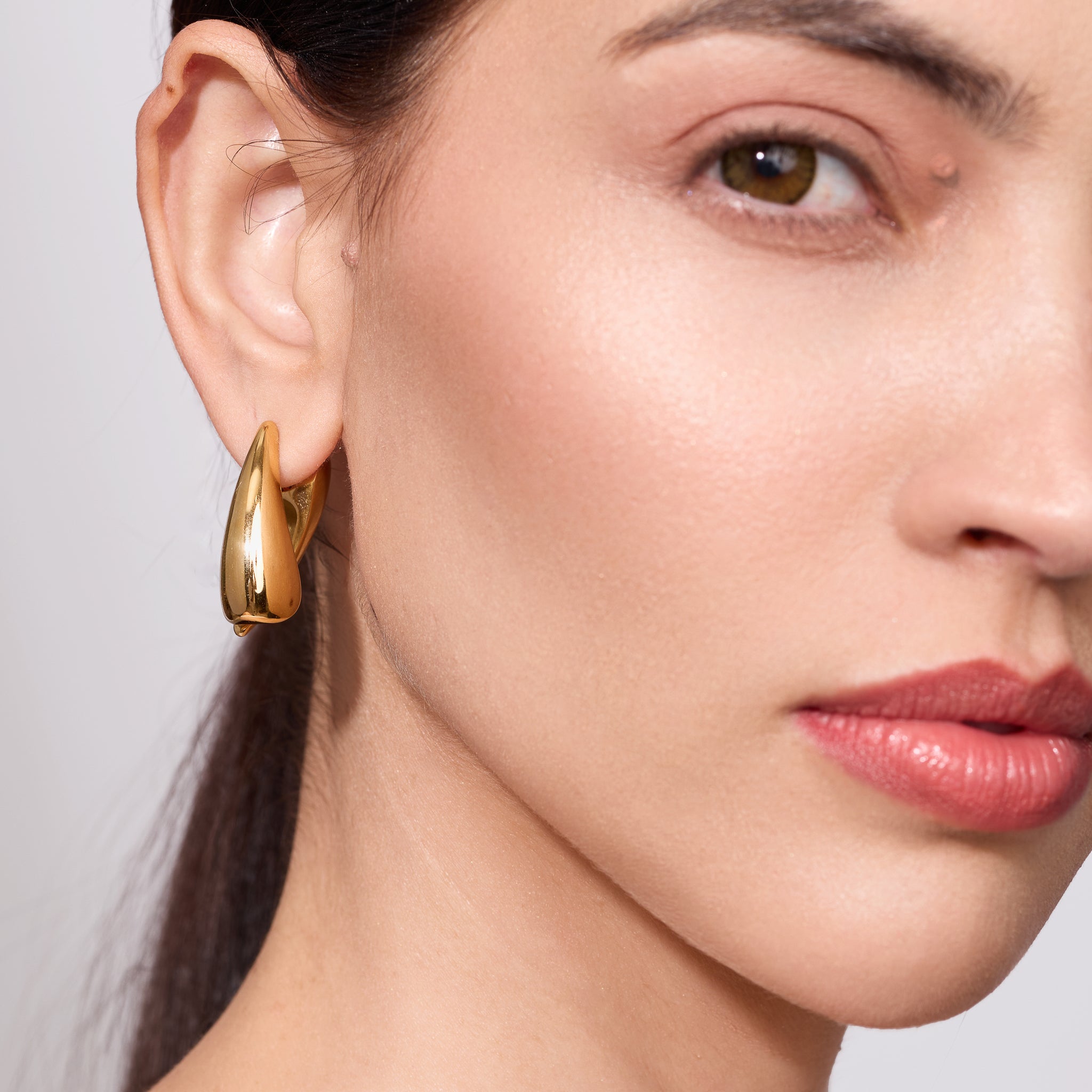 Close-up of a woman wearing a gold earring with a neutral background