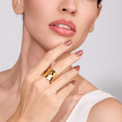 Woman wearing a 18K gold plated ring on her finger with a plain background