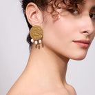 Close-up of a woman wearing gold earrings with pearl drops on a neutral background