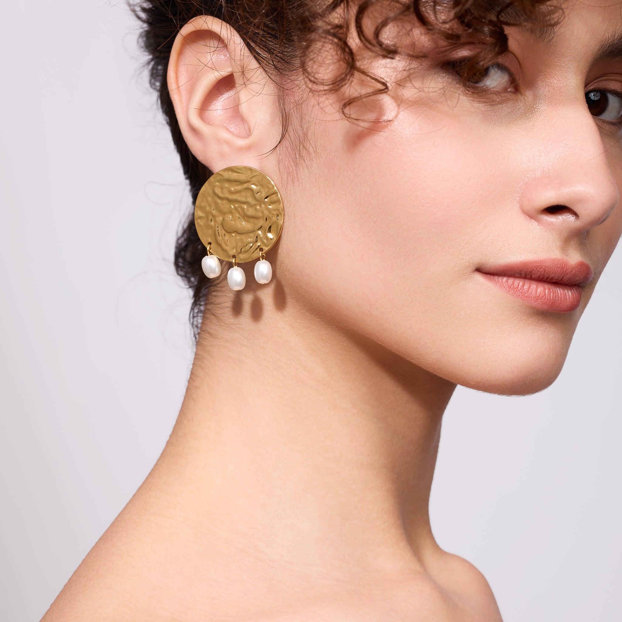 Close-up of a woman wearing gold earrings with pearl drops on a neutral background